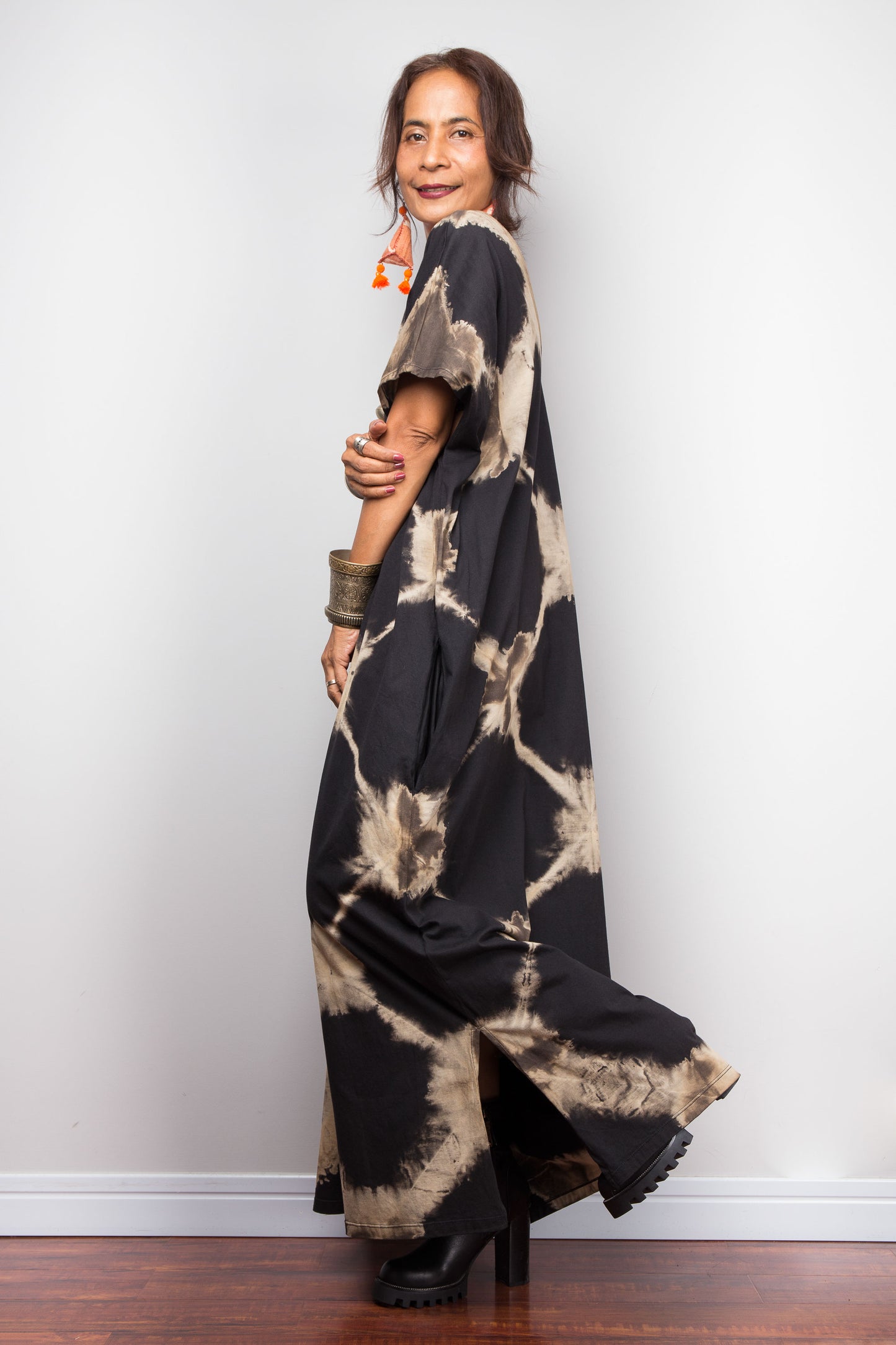 Woman wearing a black and beige tie-dye dress against a white wall.