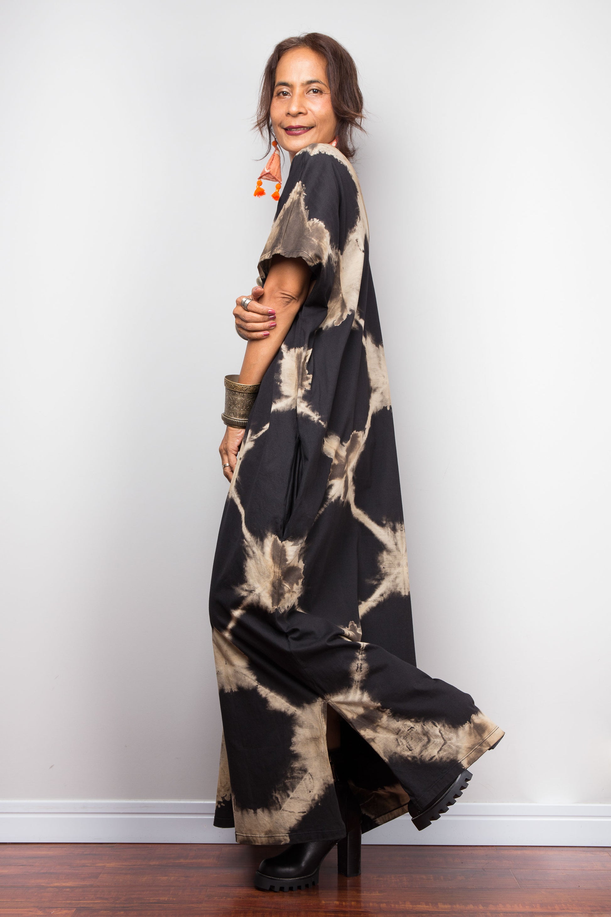 Woman wearing a black and beige tie-dye dress against a white wall.