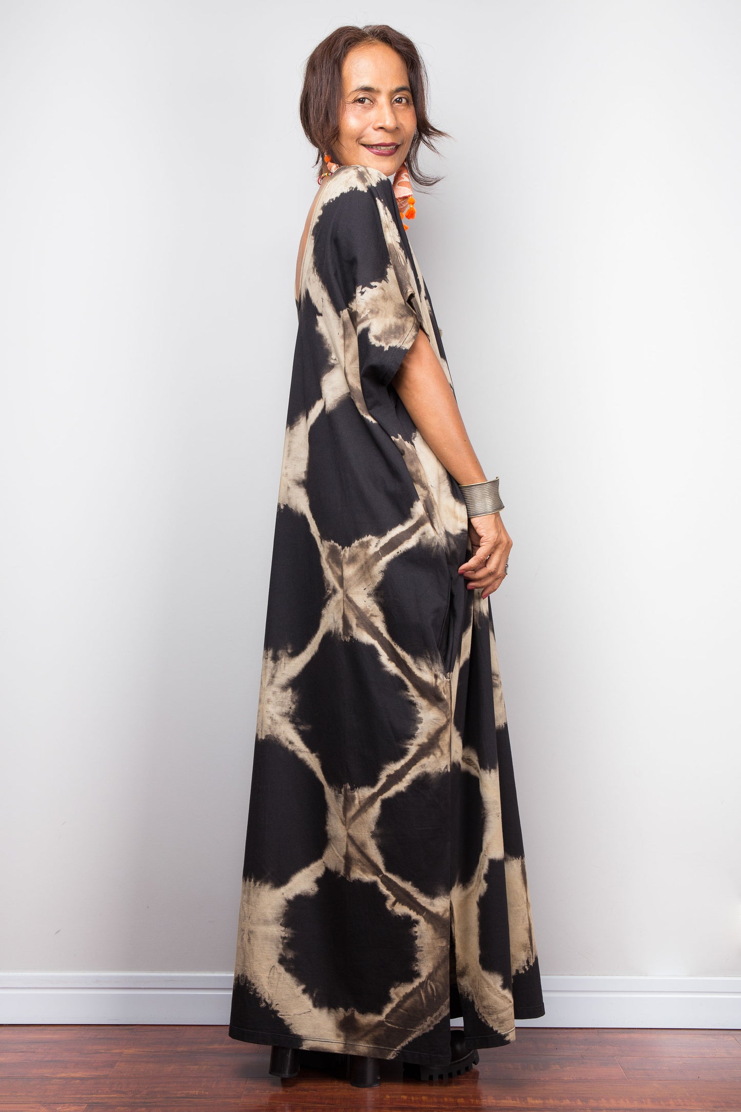 Woman wearing a long, patterned black tie dye dress against a plain background
