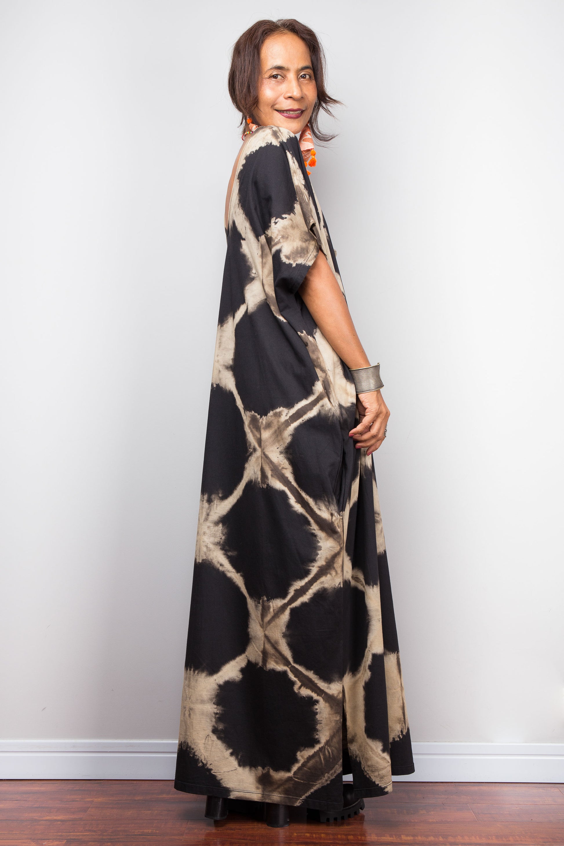 Woman wearing a long, patterned black tie dye dress against a plain background