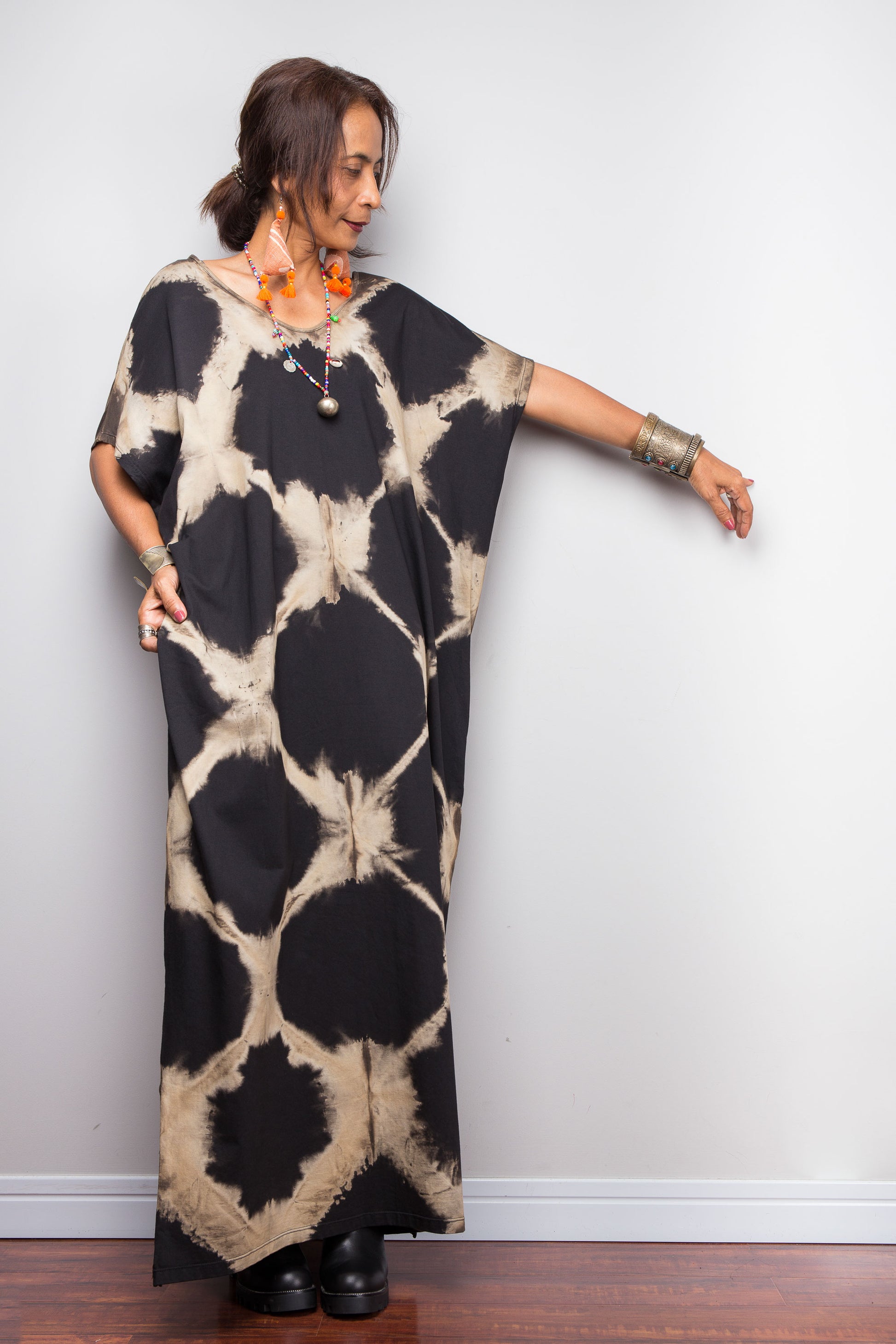 Woman wearing a black and beige tie dye kaftan dress against a plain wall.