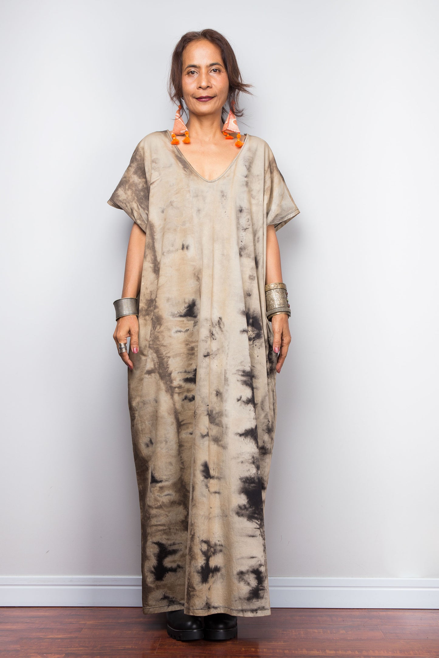 Full front view of a petite model in an authentic Nuichan brand reverse tie dye kaftan maxi dress, featuring a soft sand and beige canvas with dark abstract bleeding patterns and a V-neckline.
