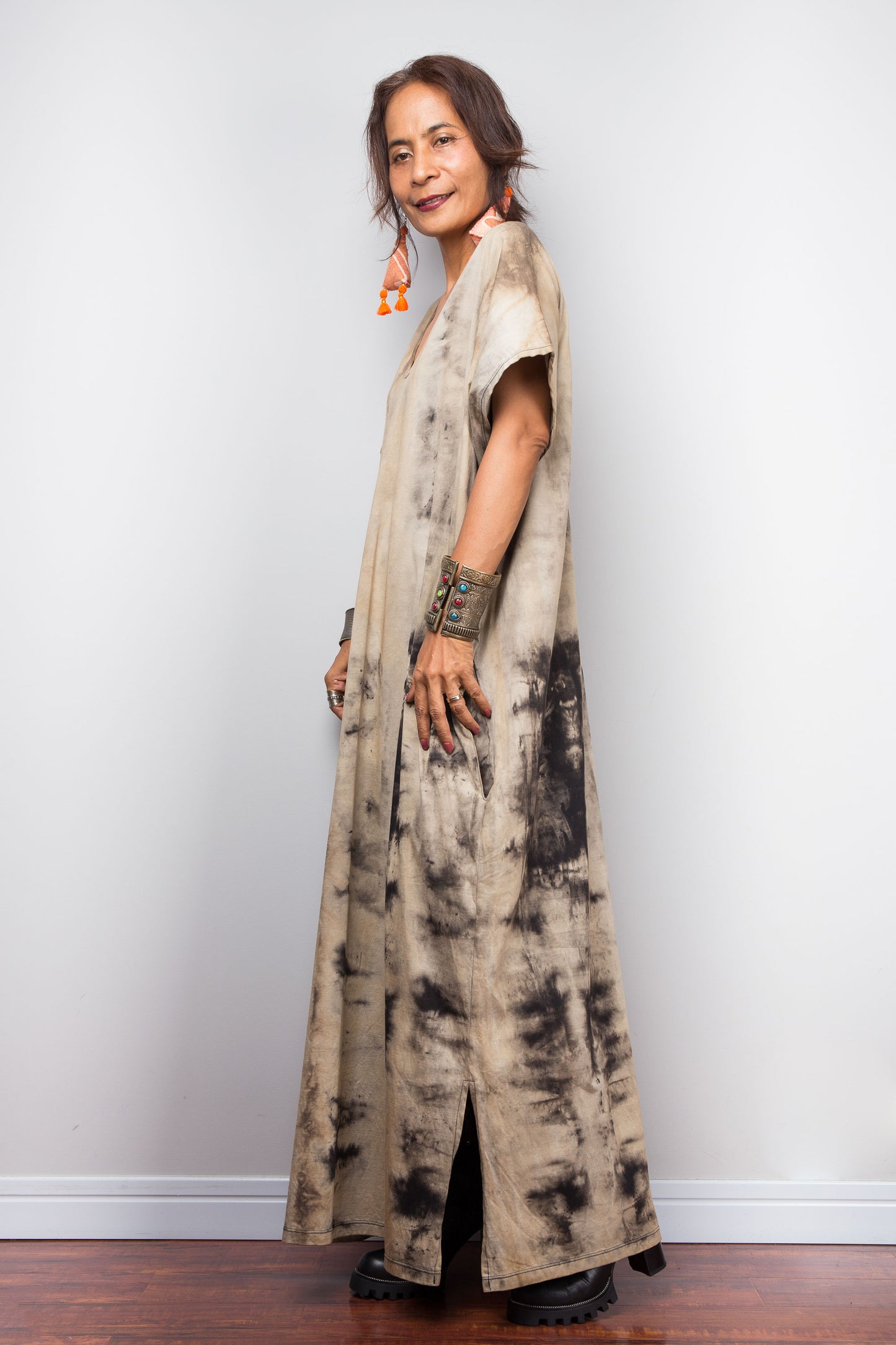 Full side view of a model in an authentic Nuichan brand reverse tie-dye kaftan maxi dress, featuring a soft sand and beige canvas with dark abstract watercolor bleeding patterns and a V-neckline and split at the hem