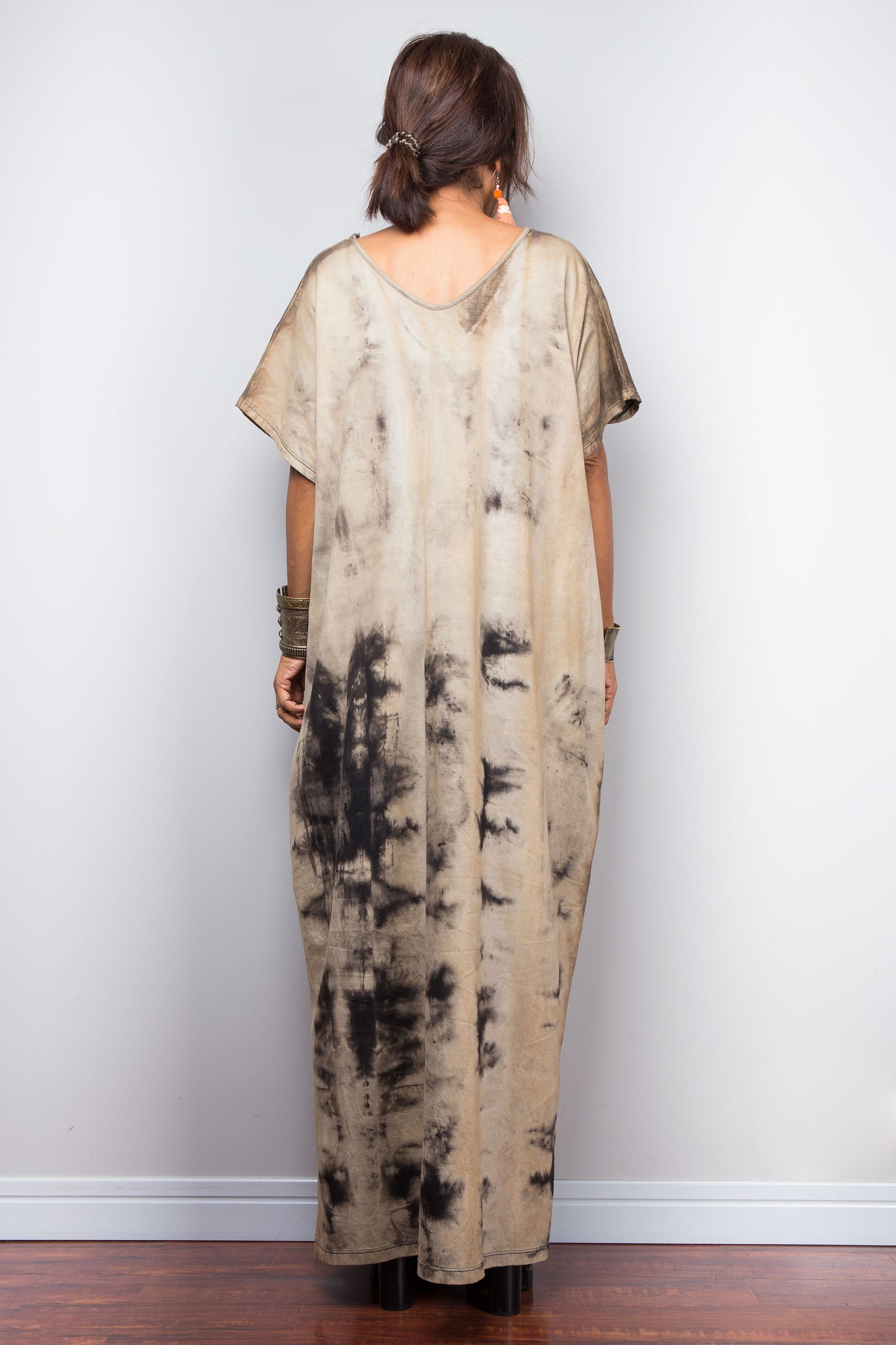 Full rear view of a model in an authentic Nuichan brand reverse tie-dye kaftan maxi dress, featuring a soft sand and beige canvas with dark abstract watercolor bleeding patterns and a V-neckline.