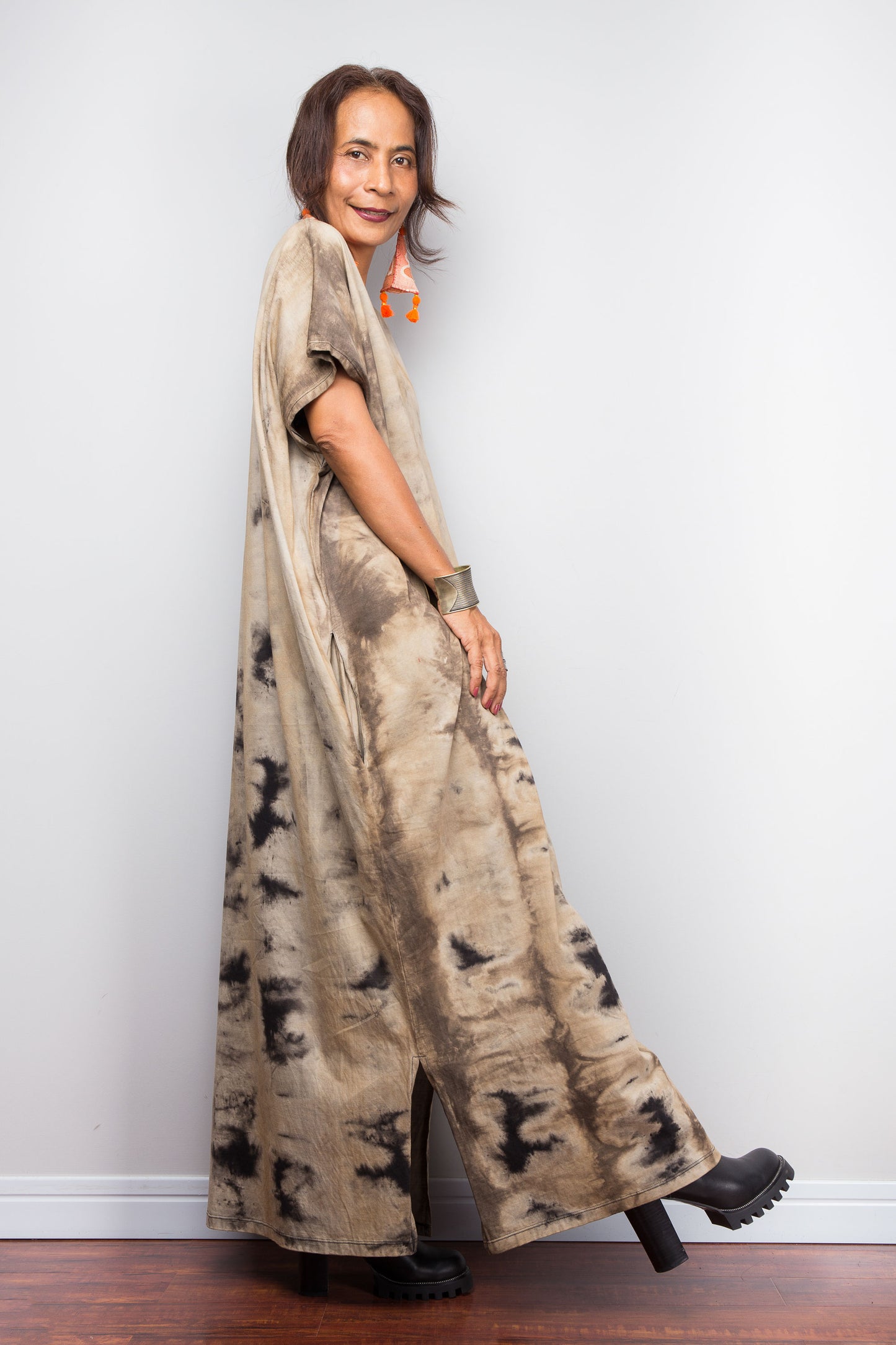 Full side view of a petite female model in an authentic Nuichan brand reverse tie-dye kaftan maxi dress, featuring a soft sand and beige canvas with dark abstract watercolor bleeding patterns and a V-neckline and side split at hem