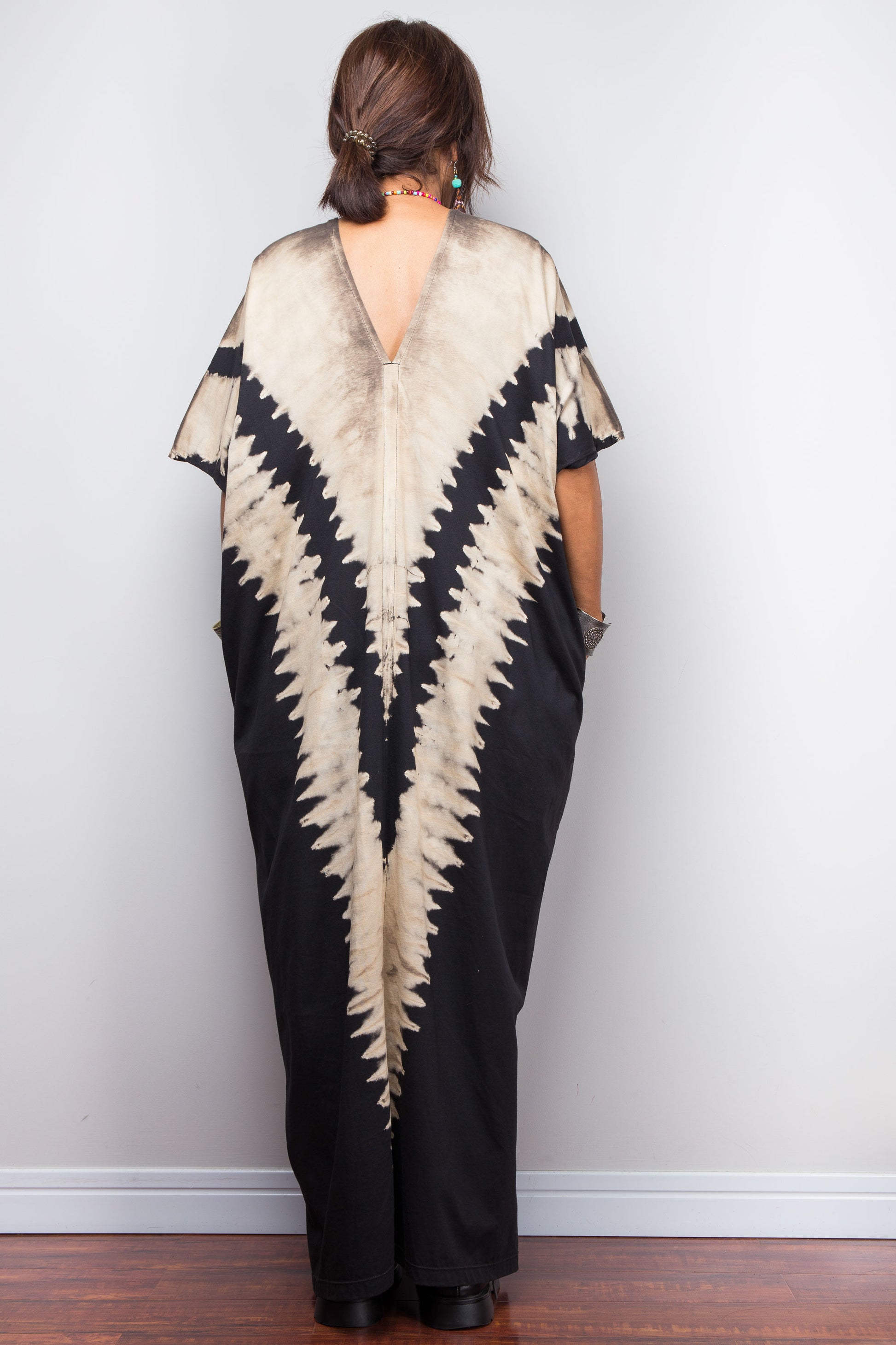 Authentic Nuichan brand oversized black and sand reverse tie dye kaftan dress, a cotton boho maxi dress with short sleeves and pockets worn by a petite model, showing the back of the dress