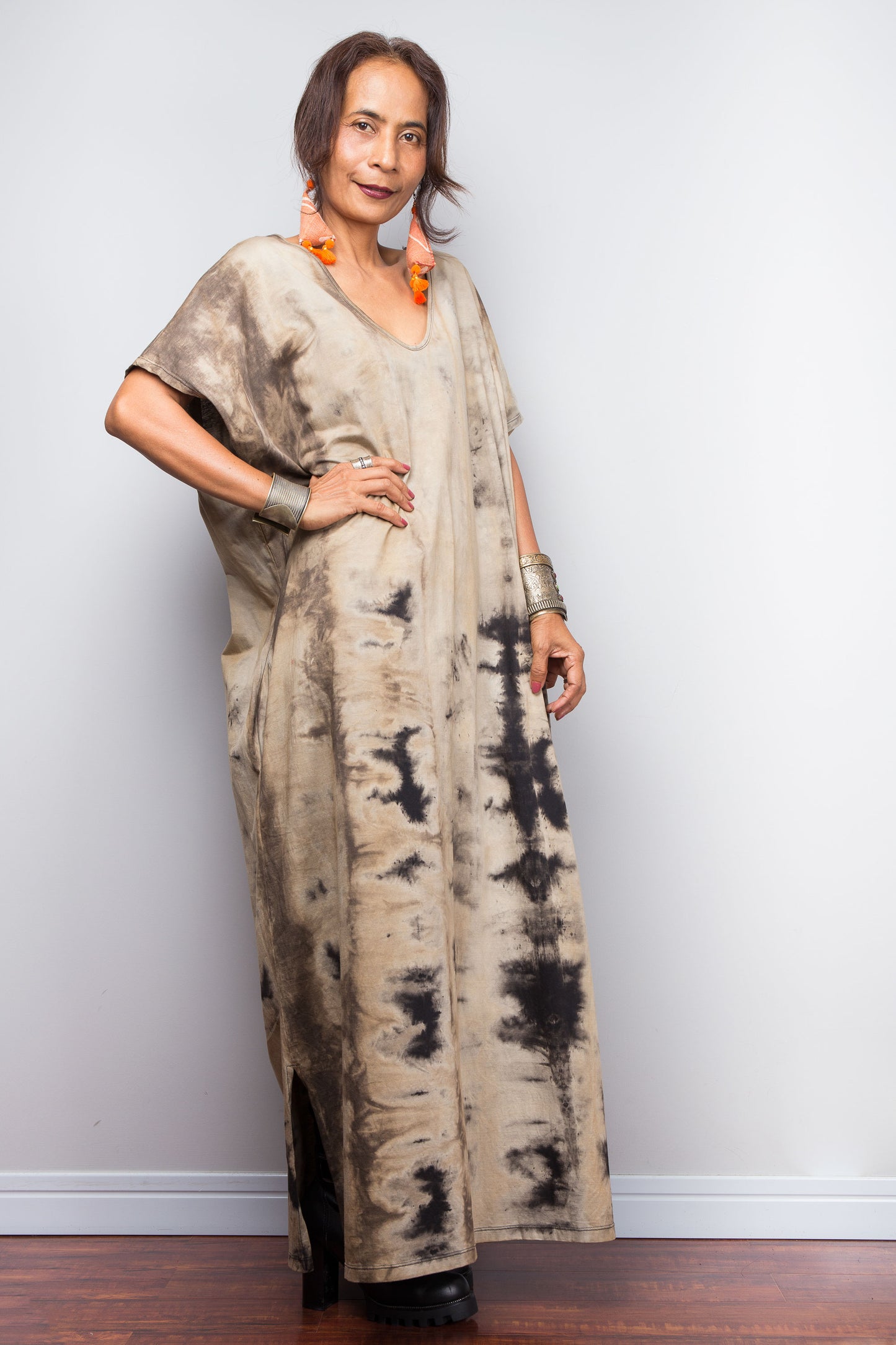 Front view of a model in an authentic Nuichan brand reverse tie-dye kaftan maxi dress, featuring a soft sand and beige canvas with dark abstract watercolor bleeding patterns and a V-neckline.