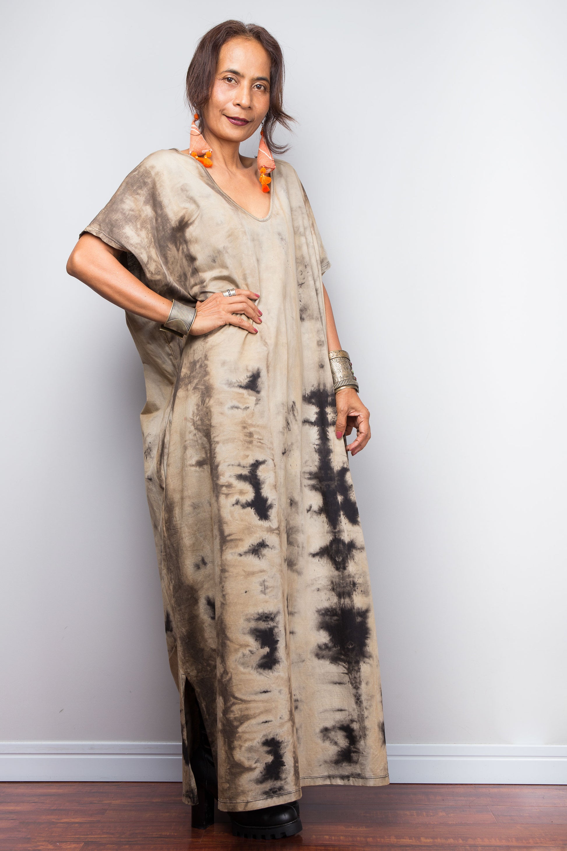 Front view of a model in an authentic Nuichan brand reverse tie-dye kaftan maxi dress, featuring a soft sand and beige canvas with dark abstract watercolor bleeding patterns and a V-neckline.