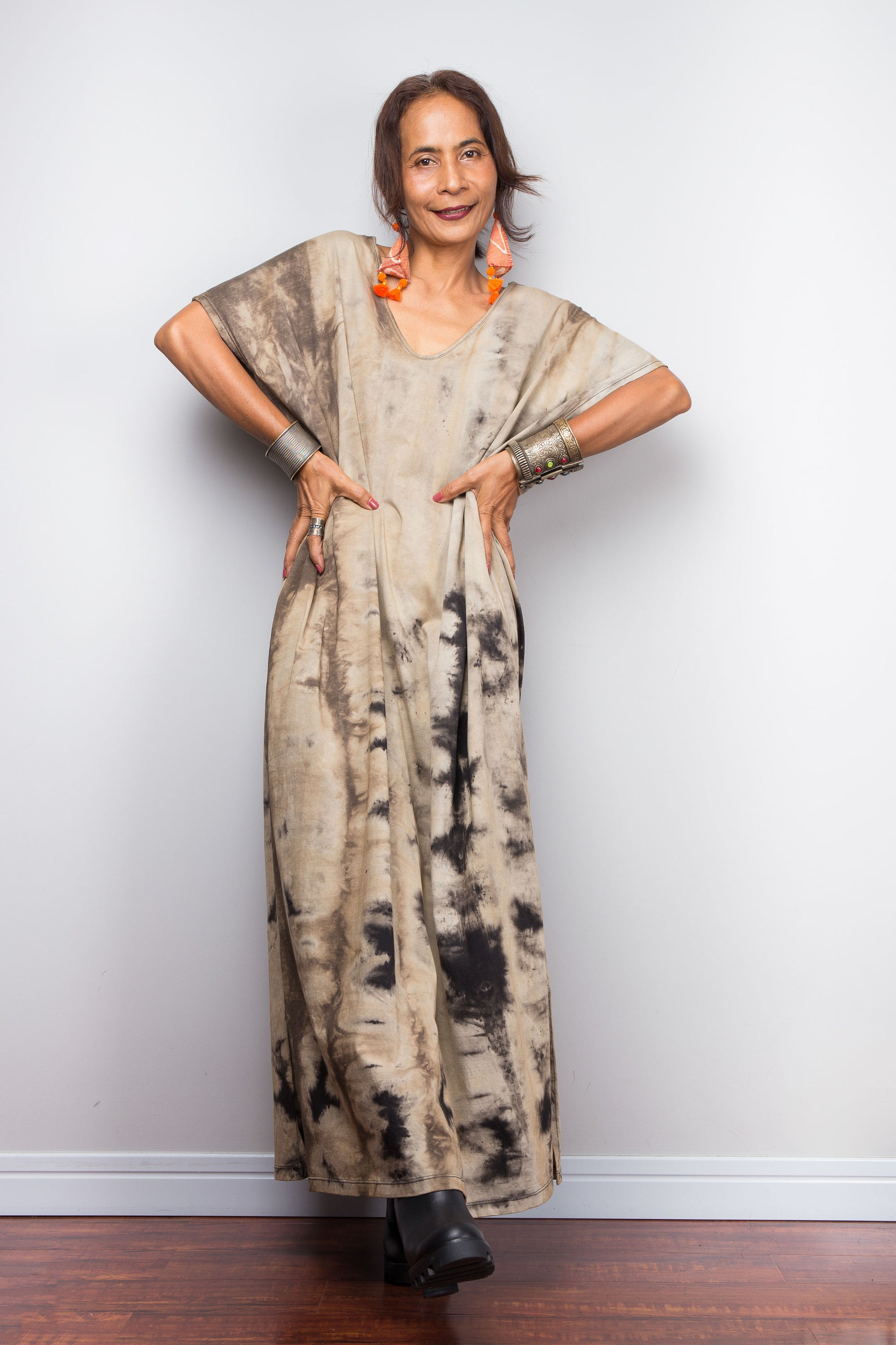 Front view of a model in an authentic Nuichan brand reverse tie-dye kaftan maxi dress, featuring a soft sand and beige canvas with dark abstract watercolor bleeding patterns and a soft round V-neckline.