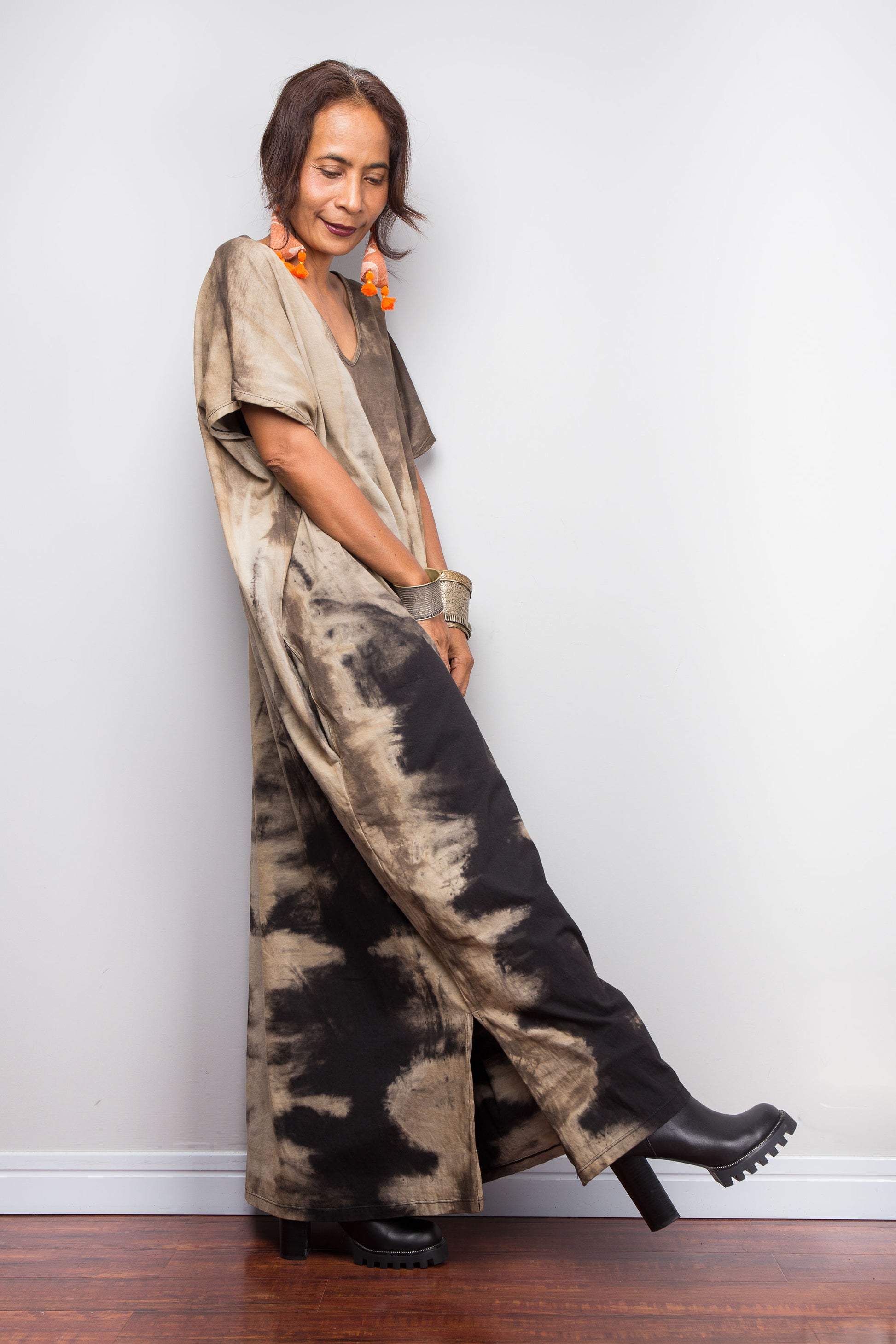Side view of a petite female model styling Nuichan's oversized reverse tie-dye kaftan dress, showcasing the loose fit, split hem and sand-colored pattern.
