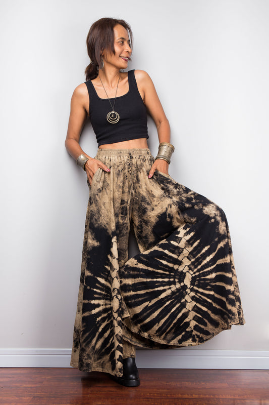 Petite Woman wearing a black top and original Nuichan reverse tie dye wide leg pants against a white wall.