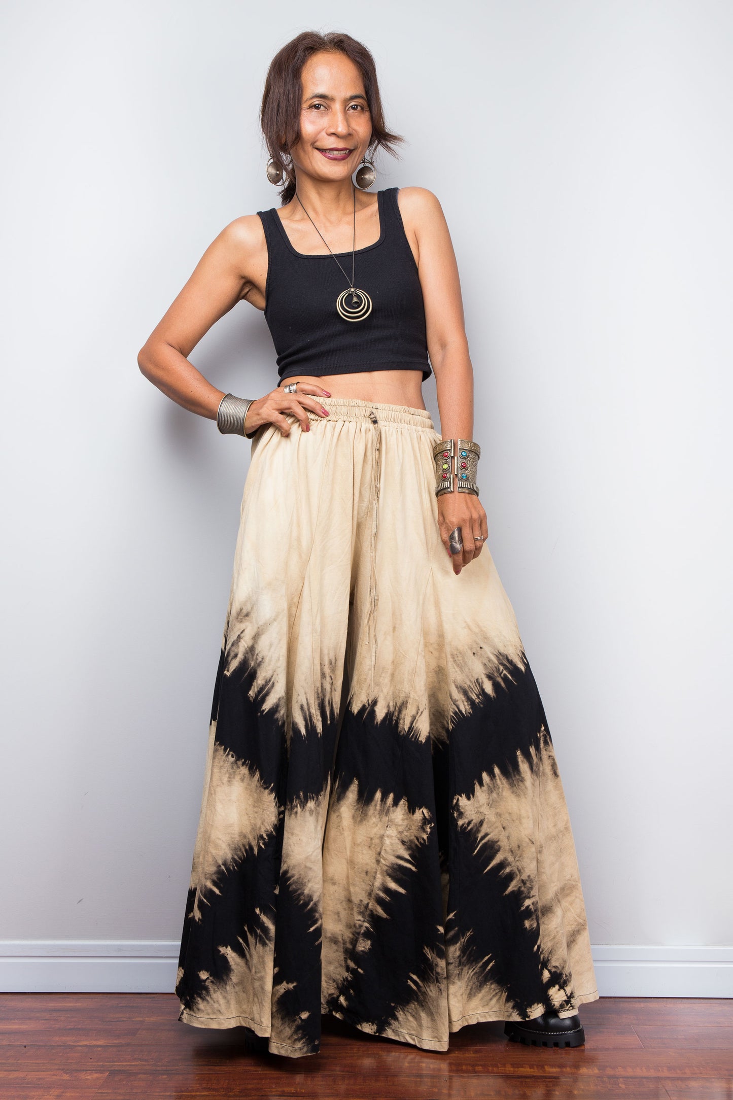 Petite Woman wearing black and beige tie dye wide leg pants against a white wall.
