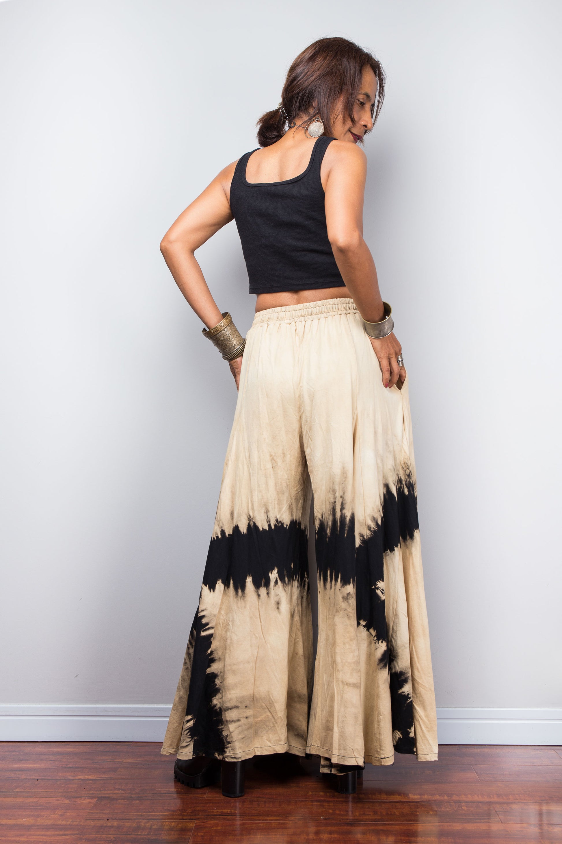 Woman wearing a black top and tie-dye wide-leg pants against a plain background