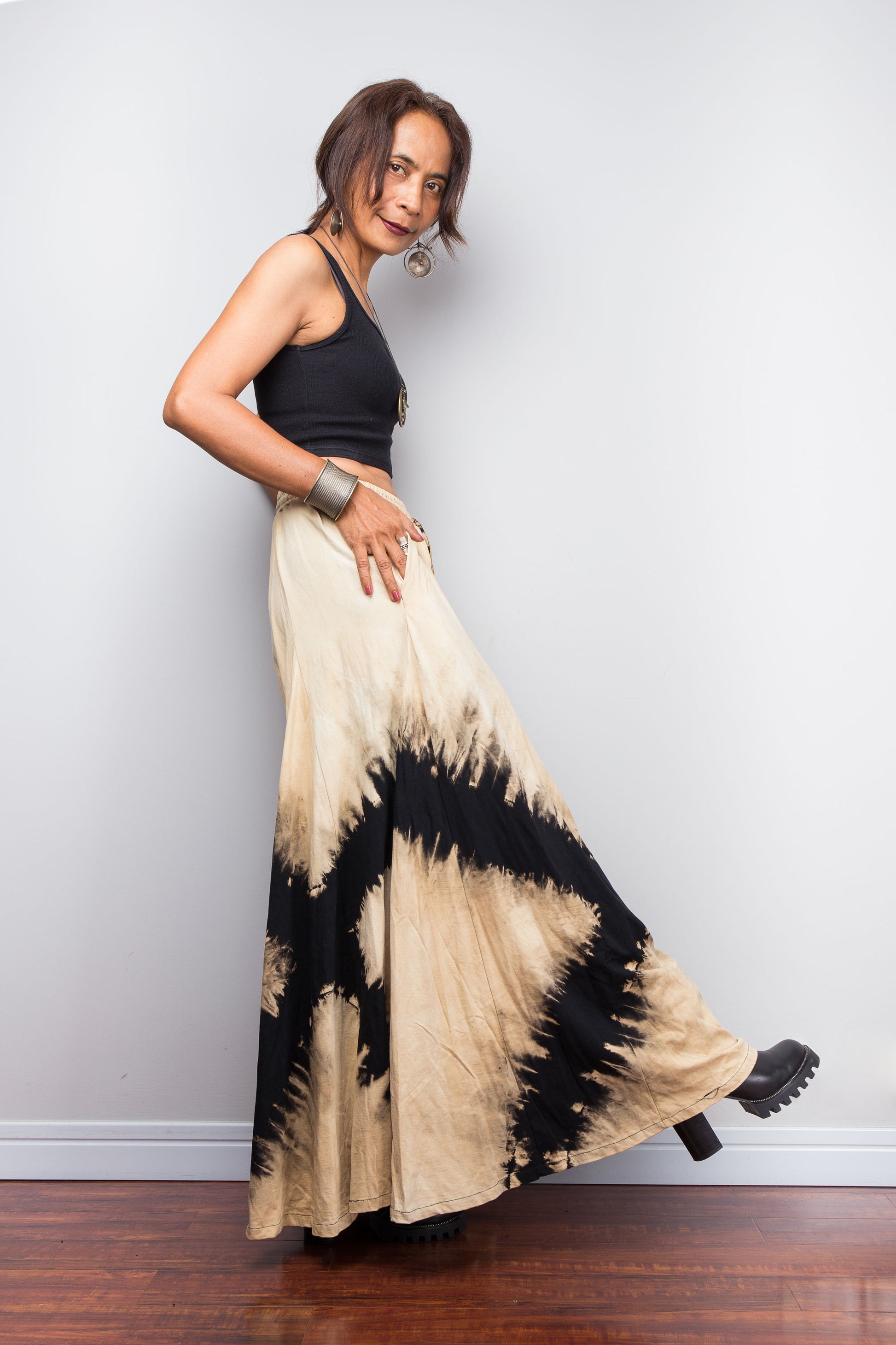 Petite Model posing dynamically to showcase the pocket and the immense fabric volume of Nuichan's oversized reverse tie dye palazzo pants, illustrating the skirt-like flow and dramatic movement of the unstructured wide legs.