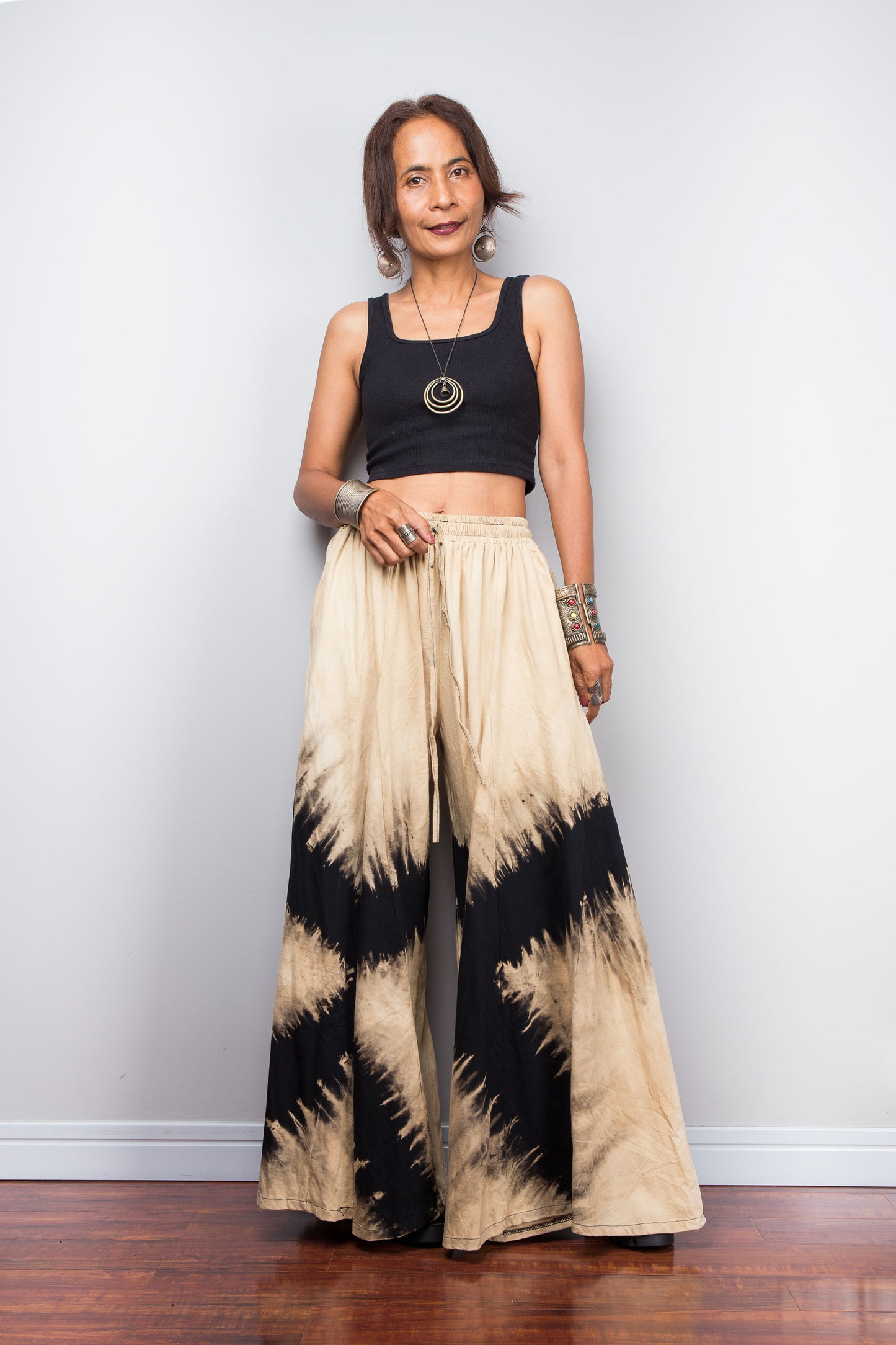 Woman wearing a black and beige, reverse tie dyed wide leg palazzo pants against a white wall background