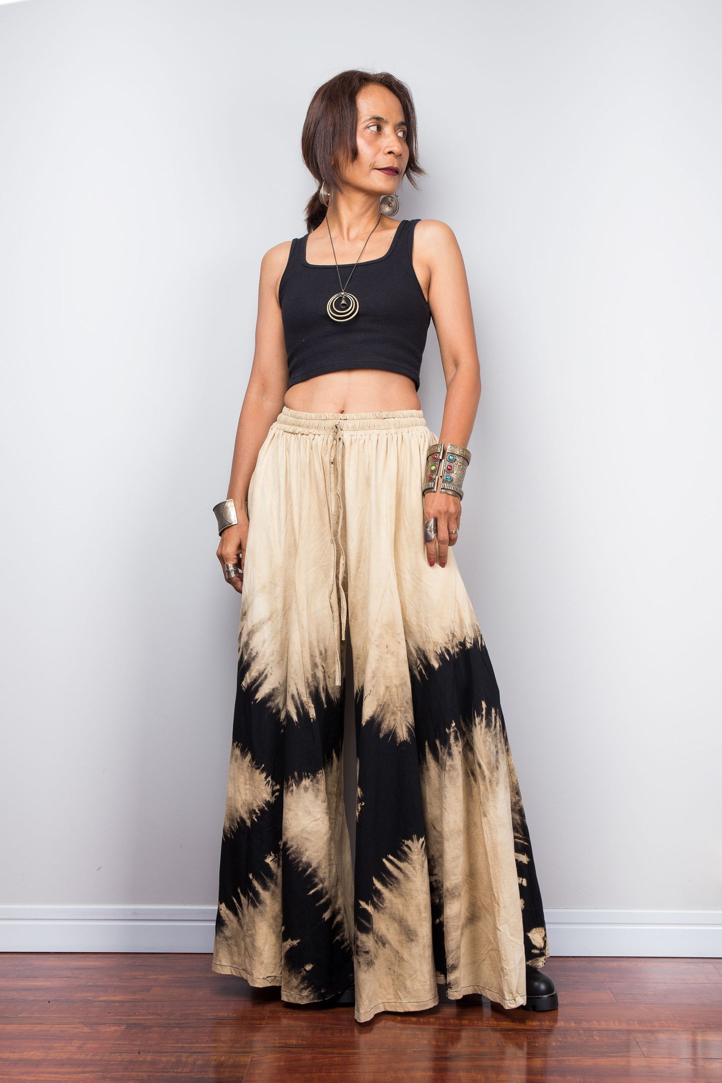 Woman wearing black and beige reverse tie-dye pants against a white wall.