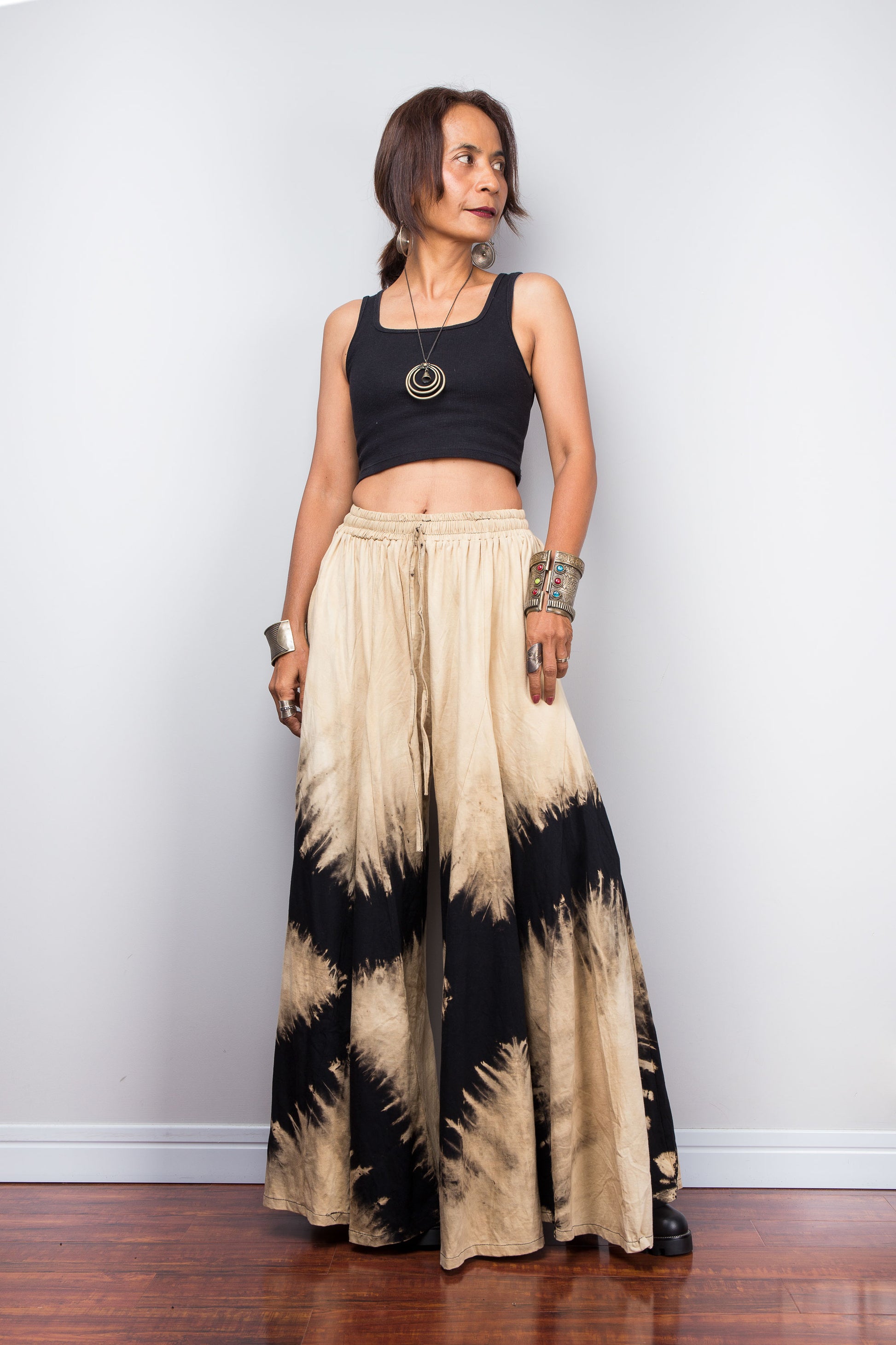 Woman wearing black and beige reverse tie-dye pants against a white wall.