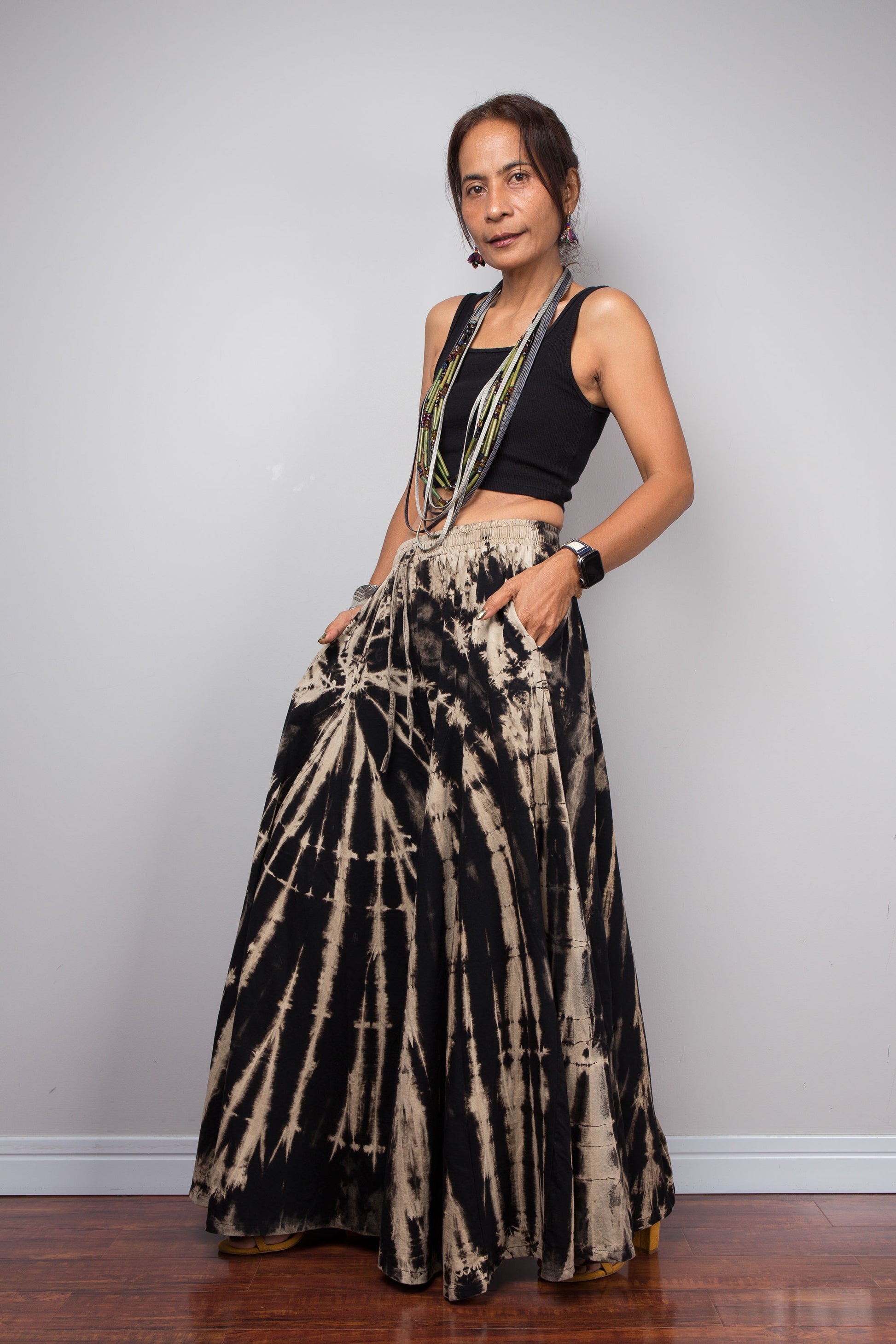Three-quarter front view of a model in the Nuichan black and sand shibori stripe reverse tie dye palazzo pants with hand in side pocket, demonstrating the functional hidden pocket detail and the immense skirt-like volume and fluid drape of the ultra-wide cotton legs