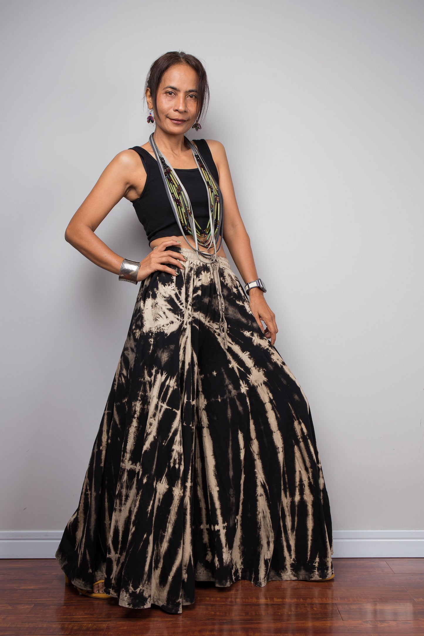 Three-quarter front view of a model in the Nuichan black and sand stripe reverse tie dye palazzo pants with hand on the hip demonstrating the immense skirt-like volume and fluid drape of the ultra-wide cotton legs