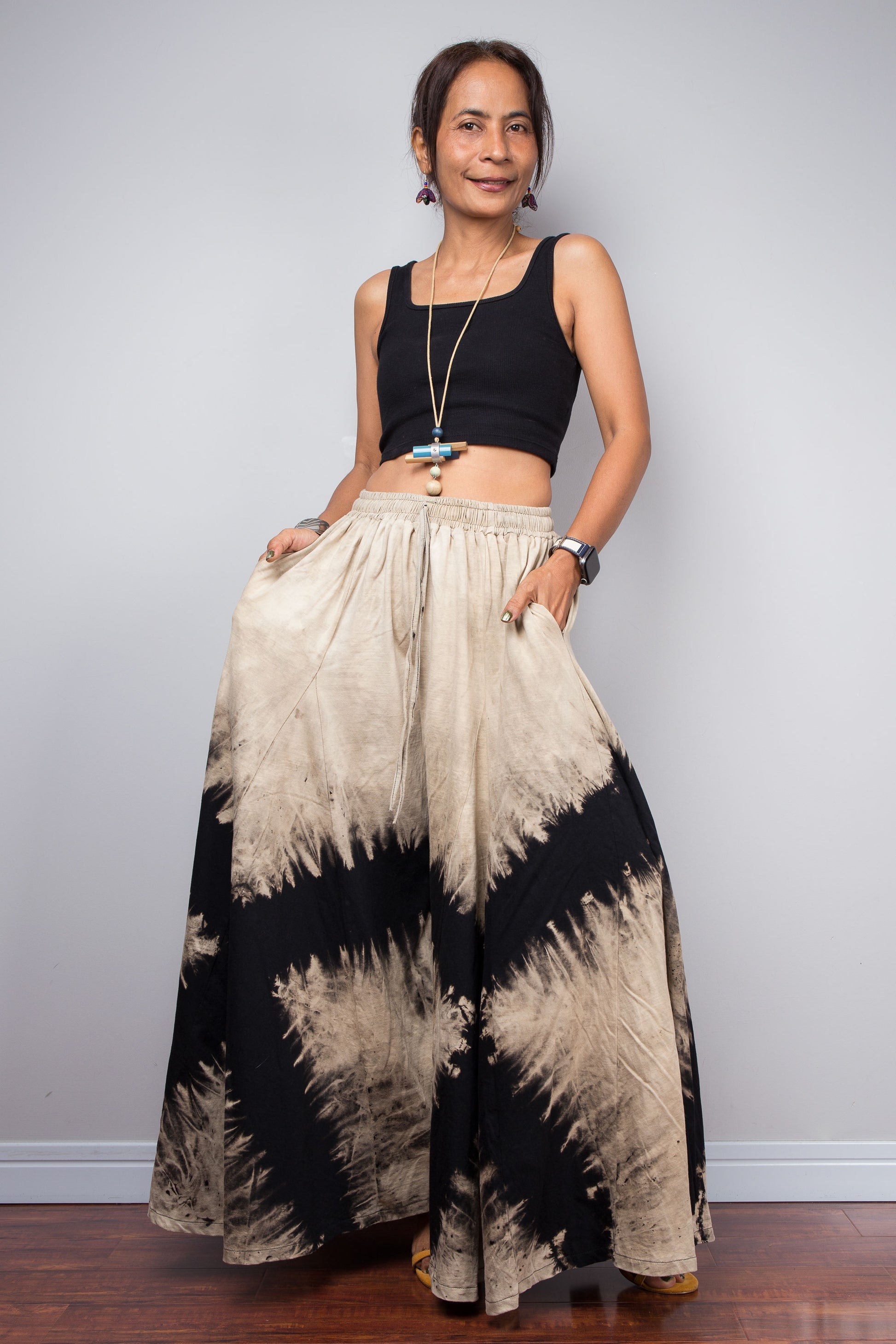Petite Model posing dynamically to showcase the immense fabric volume of Nuichan's oversized reverse tie dye palazzo pants, illustrating the skirt-like flow and dramatic movement of the unstructured wide legs.
