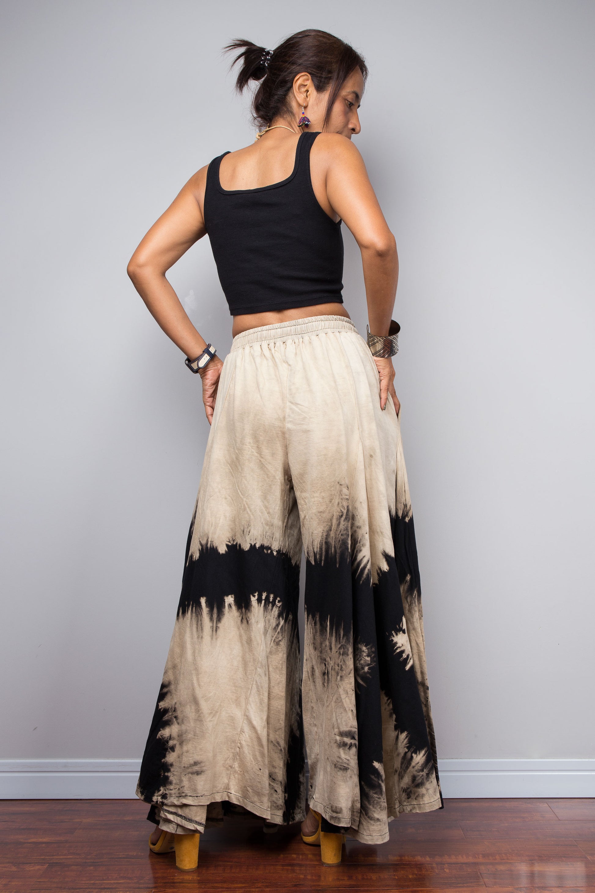 Woman wearing a black and beige, reverse tie dyed wide leg palazzo pants against a white wall background