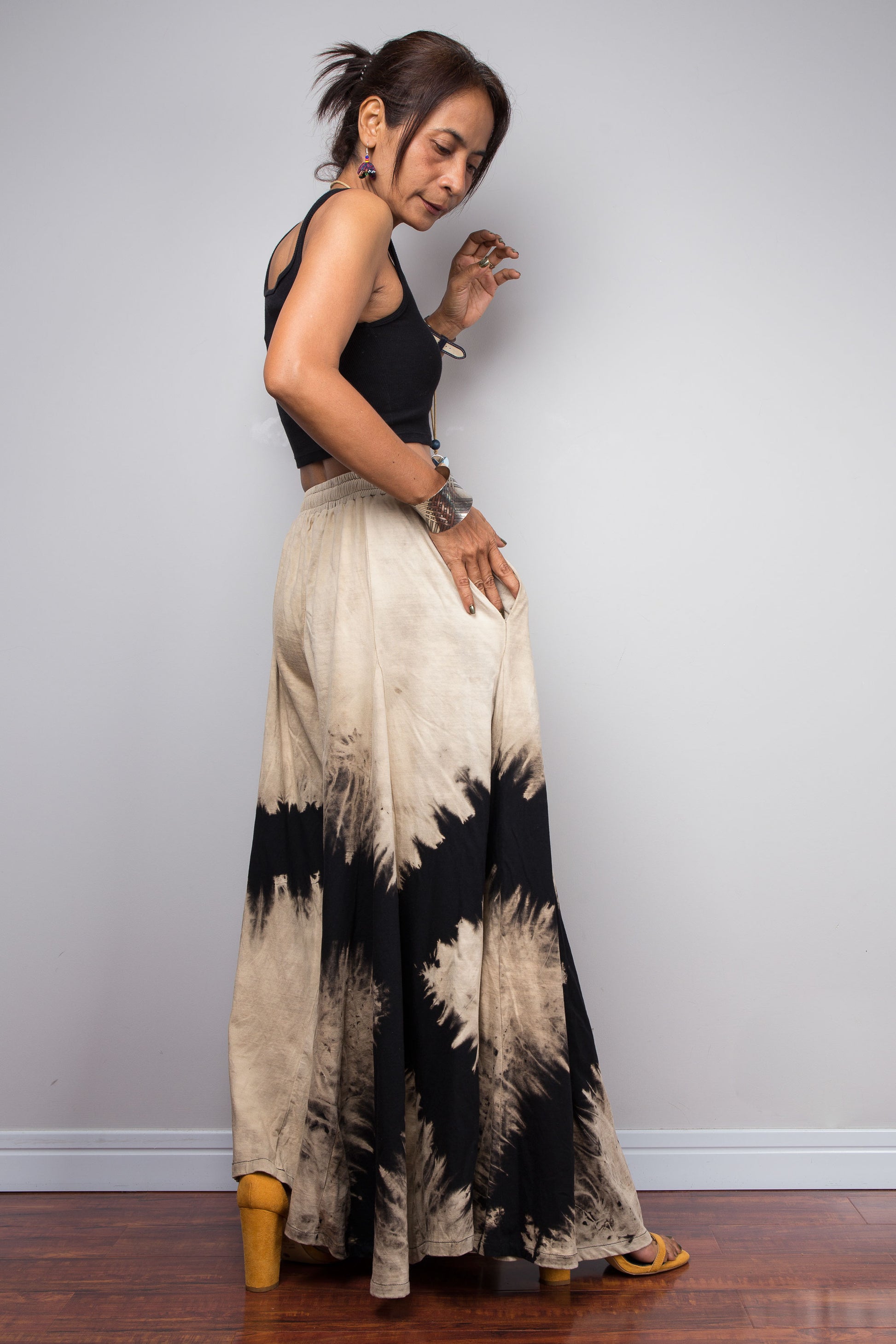 Woman wearing a black top and tie-dye wide-leg pants against a plain background