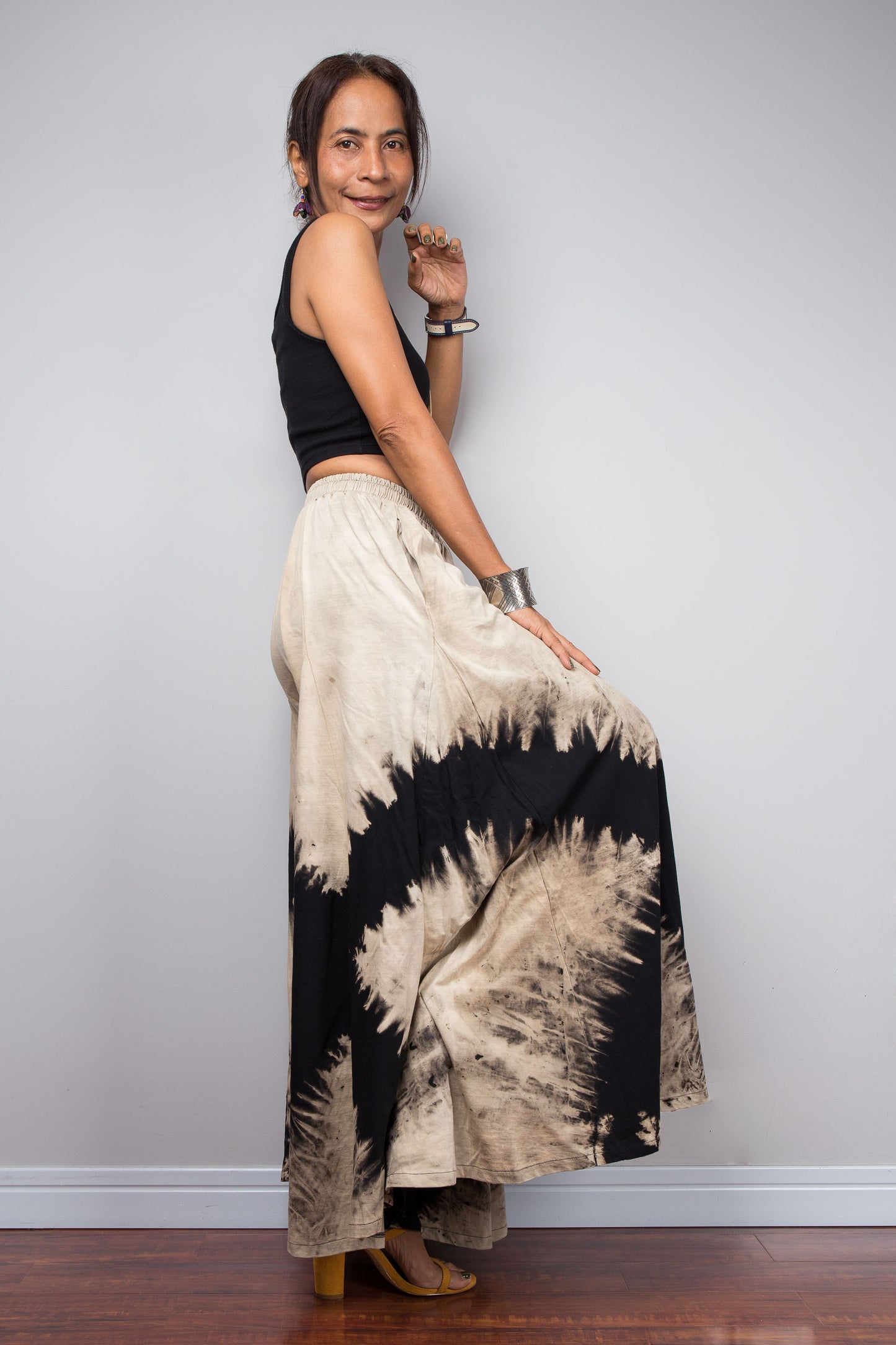 Petite Woman posing dynamically to showcase the pocket and the immense fabric volume of Nuichan's oversized reverse tie dye palazzo pants, illustrating the skirt-like flow and dramatic movement of the unstructured wide legs.