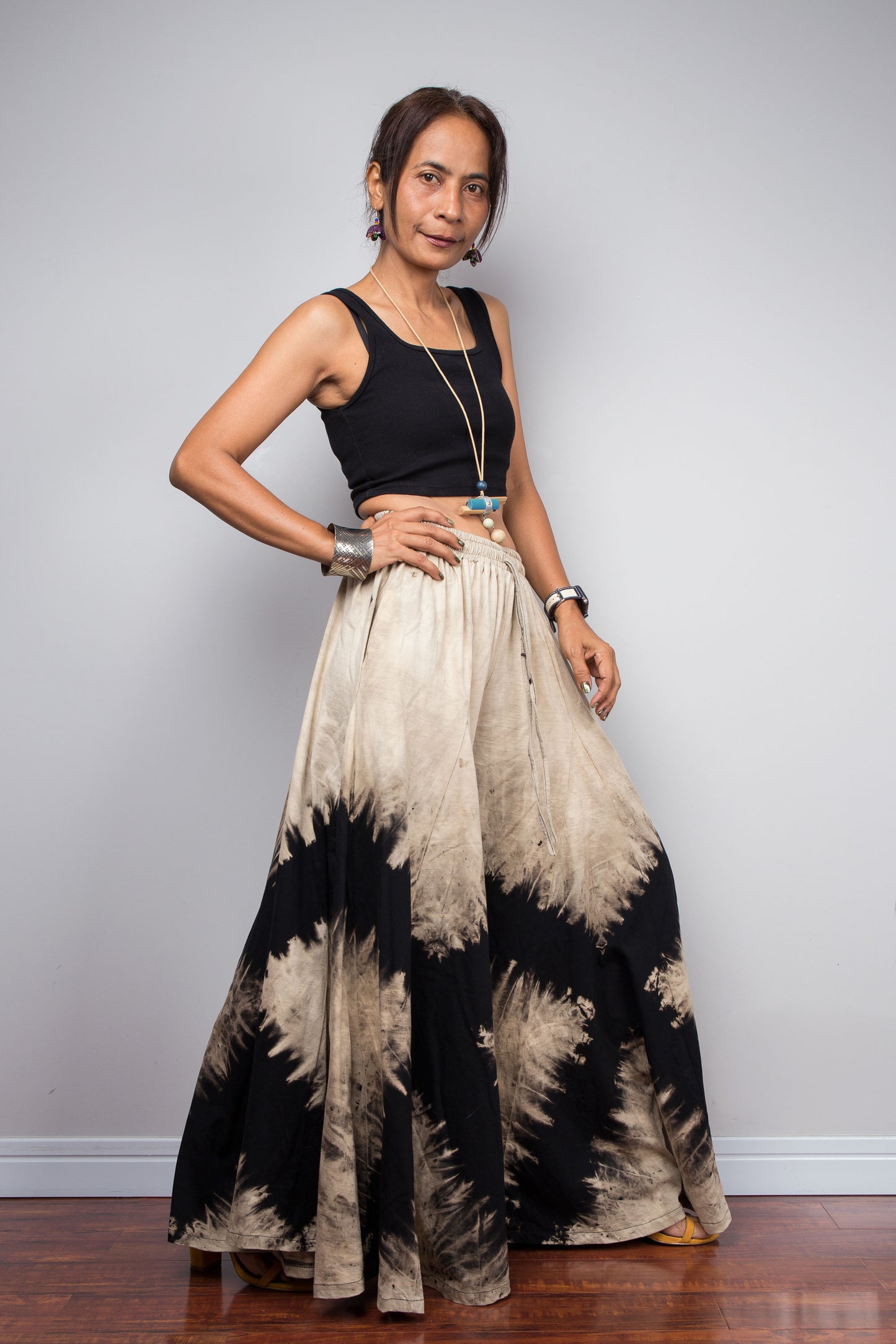 Model posing dynamically to showcase the immense fabric volume of Nuichan's oversized reverse tie dye palazzo pants, illustrating the skirt-like flow and dramatic movement of the unstructured wide legs.