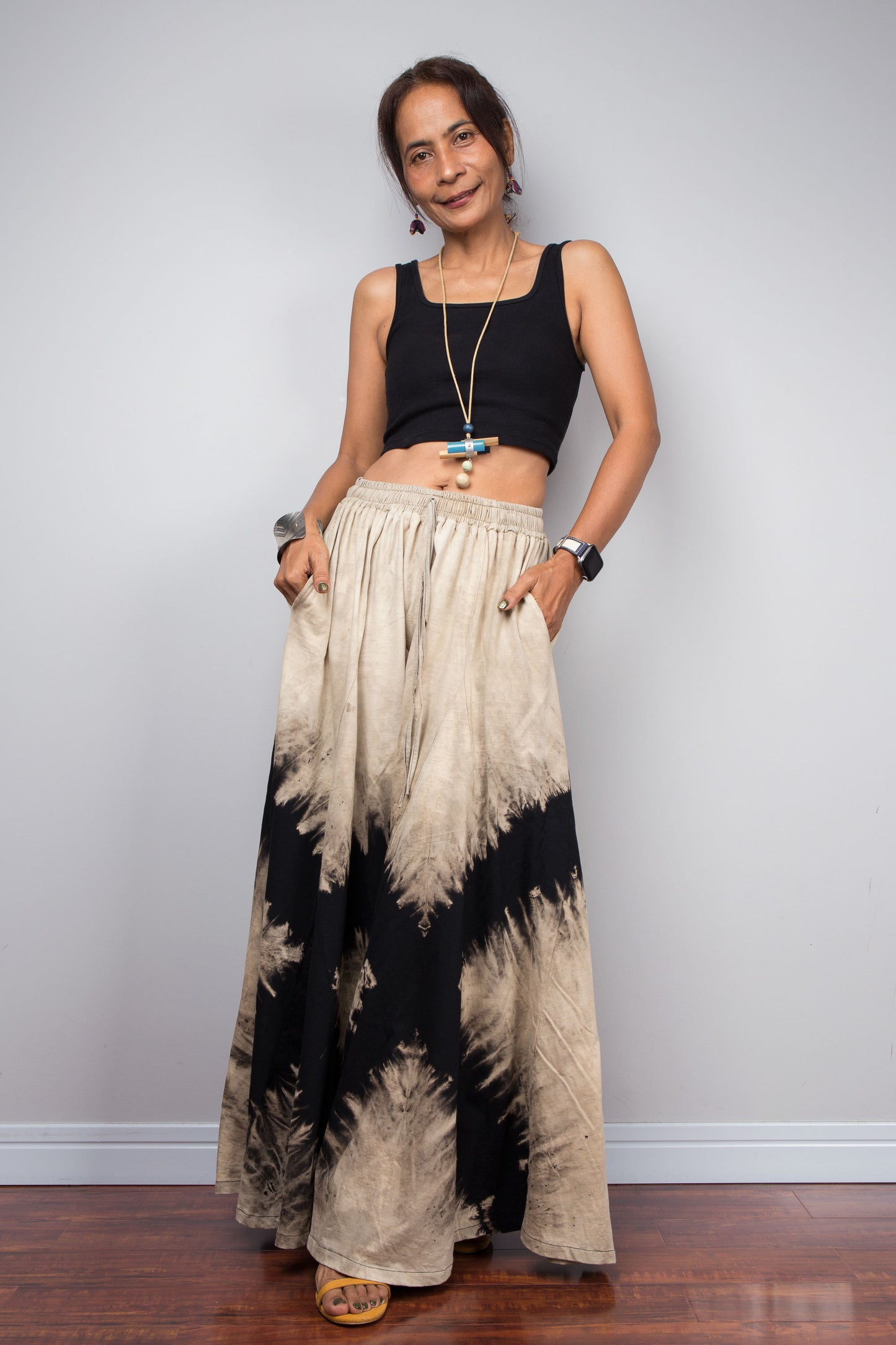 Woman wearing black and beige reverse tie-dye pants against a white wall.