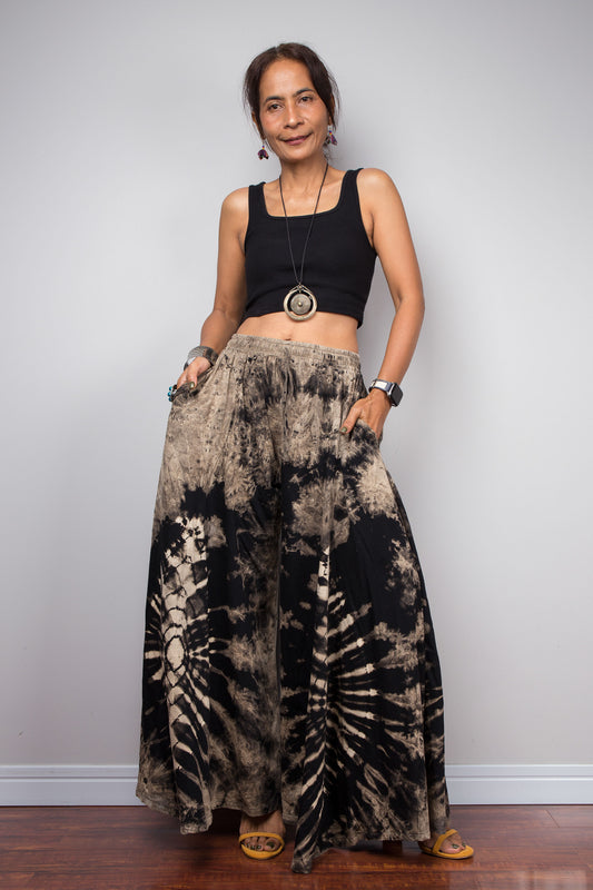 Front view of a model wearing the Nuichan reverse tie dye wide leg palazzo pants in black and sand cotton, showcasing the dramatic ultra-wide leg silhouette, high-contrast starburst pattern, and skirt-like fluid drape