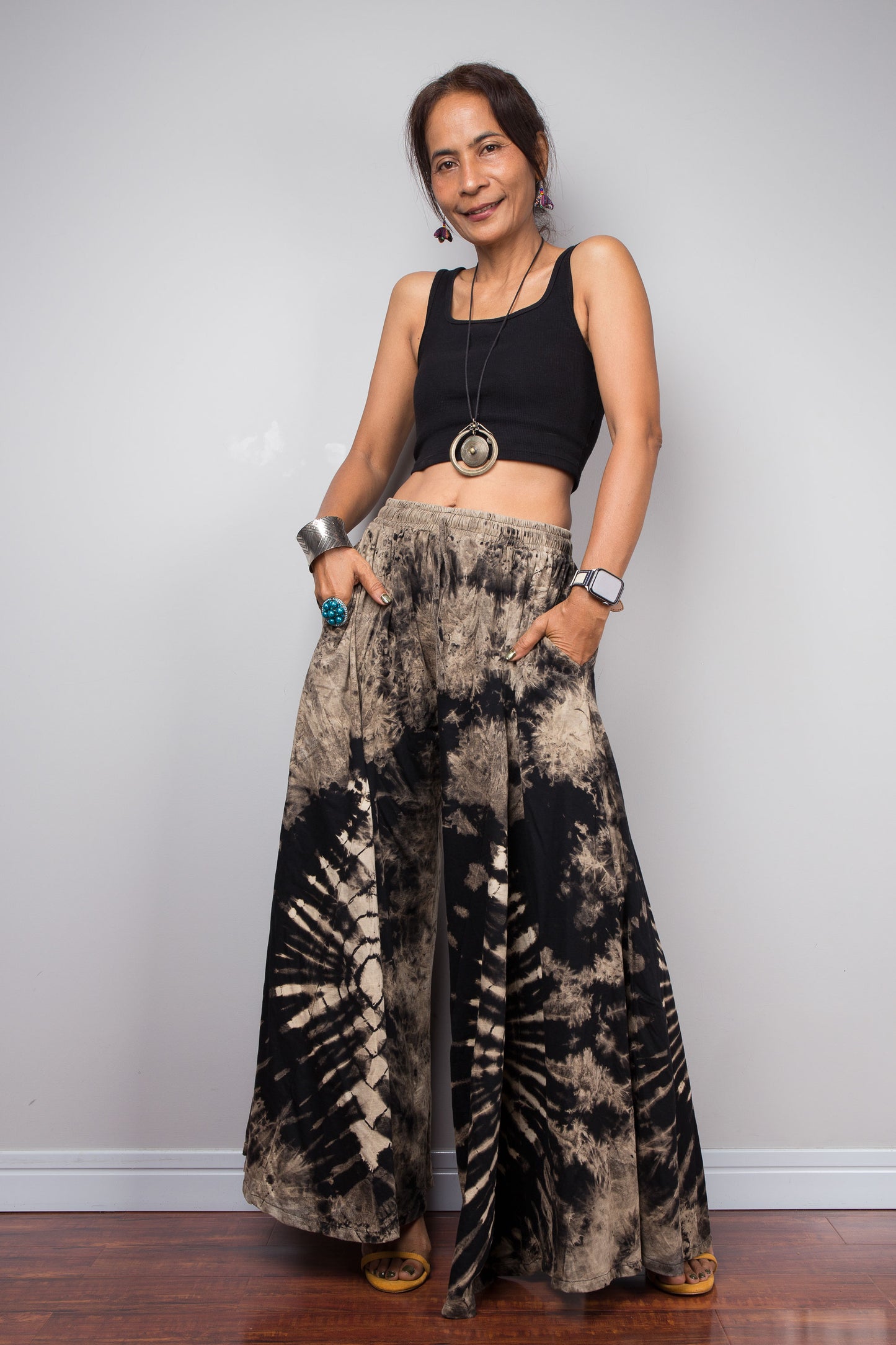 Three-quarter view of a model wearing the Nuichan reverse tie dye wide leg pants, highlighting the bold organic starburst reverse dye pattern anchoring the lower half and the relaxed smocked drawstring waistband