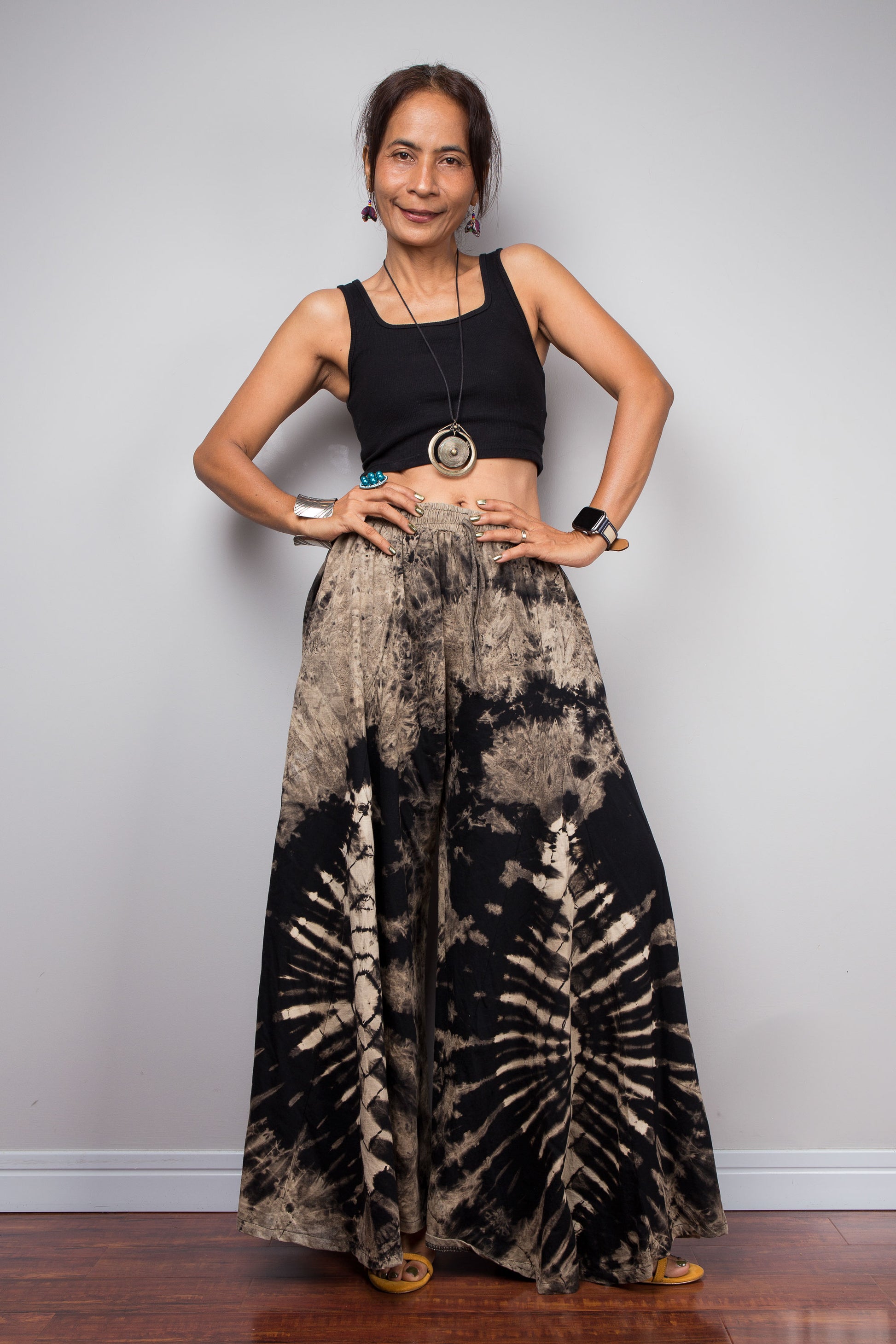 Model posing dynamically in the Nuichan reverse tie dye palazzo pants to showcase the skirt-like sweep and dramatic movement of the unstructured wide cotton legs in the black and copper sand colourway
