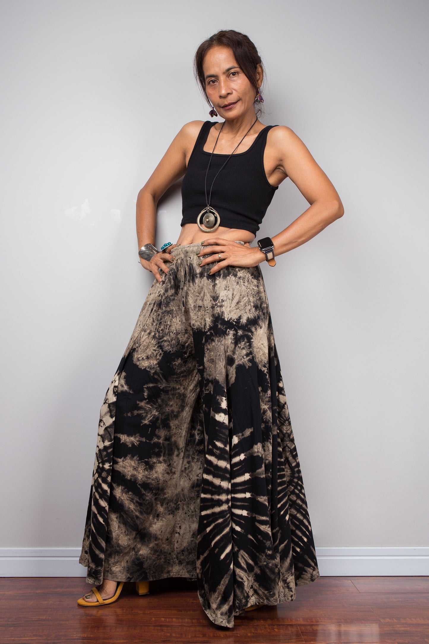 Three-quarter side view of a model in the Nuichan reverse tie dye palazzo pants, showing the flexible elastic smocked waistband, adjustable drawstring, and voluminous wide leg drape in black and sand cotton