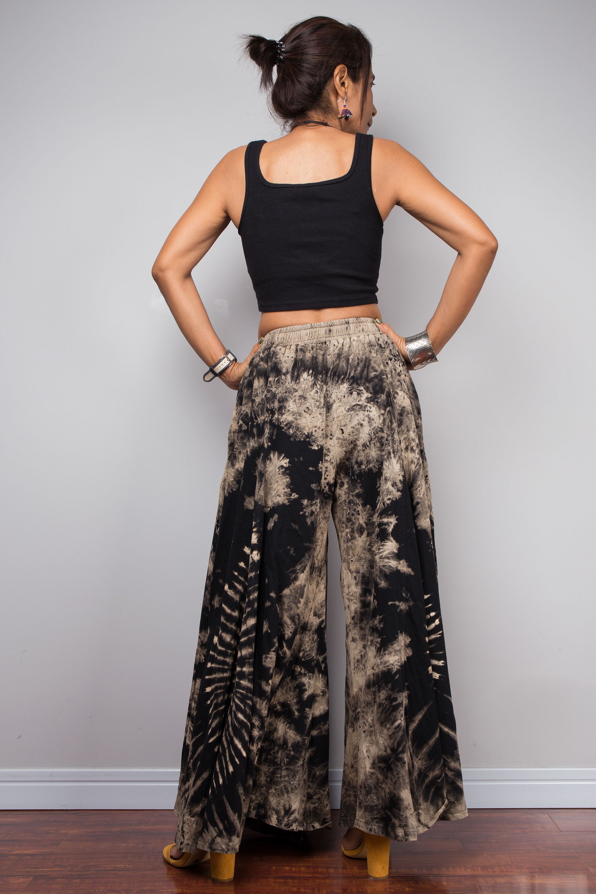Rear view of a model wearing the Nuichan black and sand reverse dye wide leg palazzo pants, displaying the full width of the ultra-wide leg silhouette and the continuation of the organic starburst reverse dye pattern