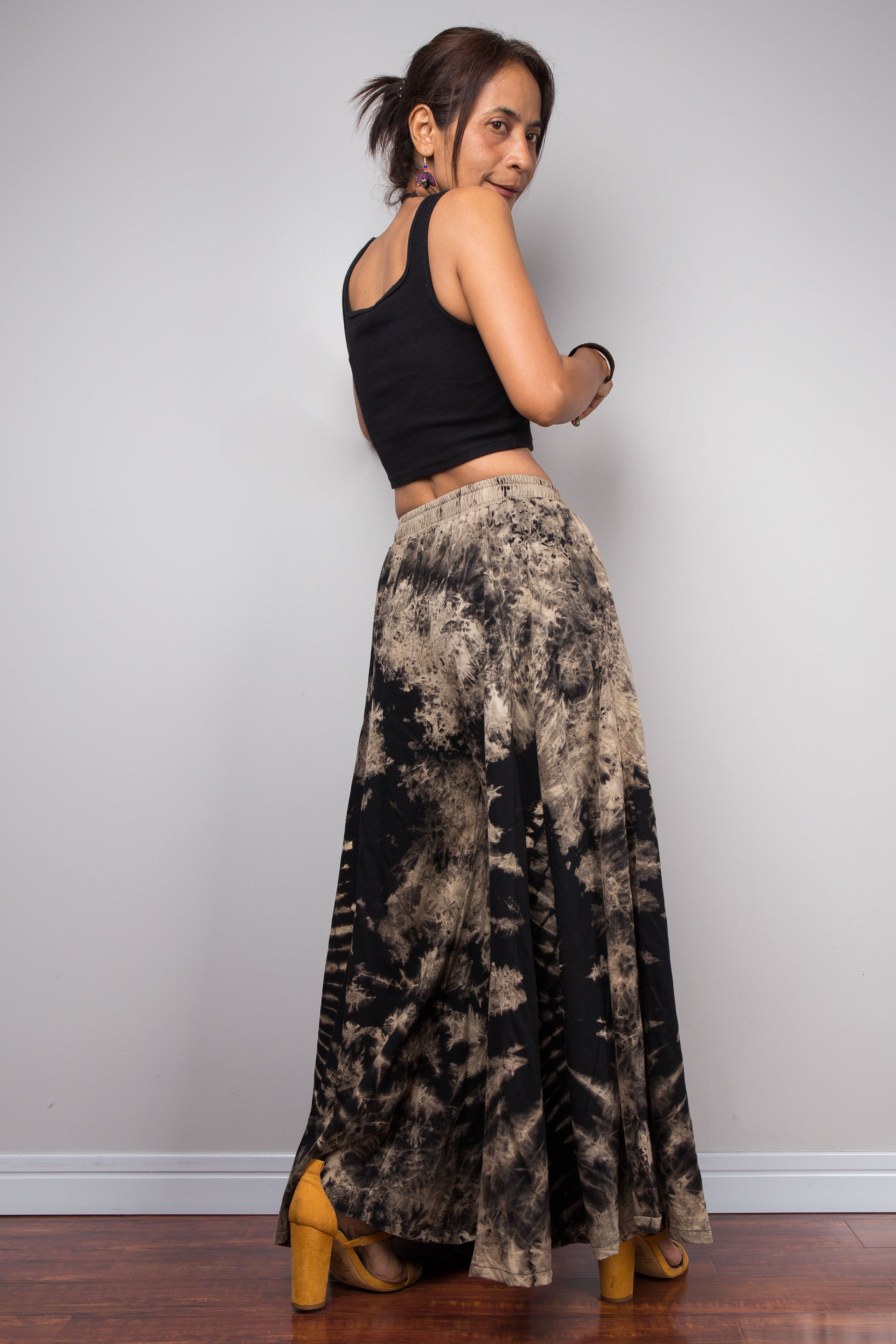 Dynamic movement shot of a model in the Nuichan reverse dye wide leg palazzo pants, capturing the dramatic skirt-like fabric volume, flowing black and copper sand cotton, and bold organic reverse tie dye pattern in motion