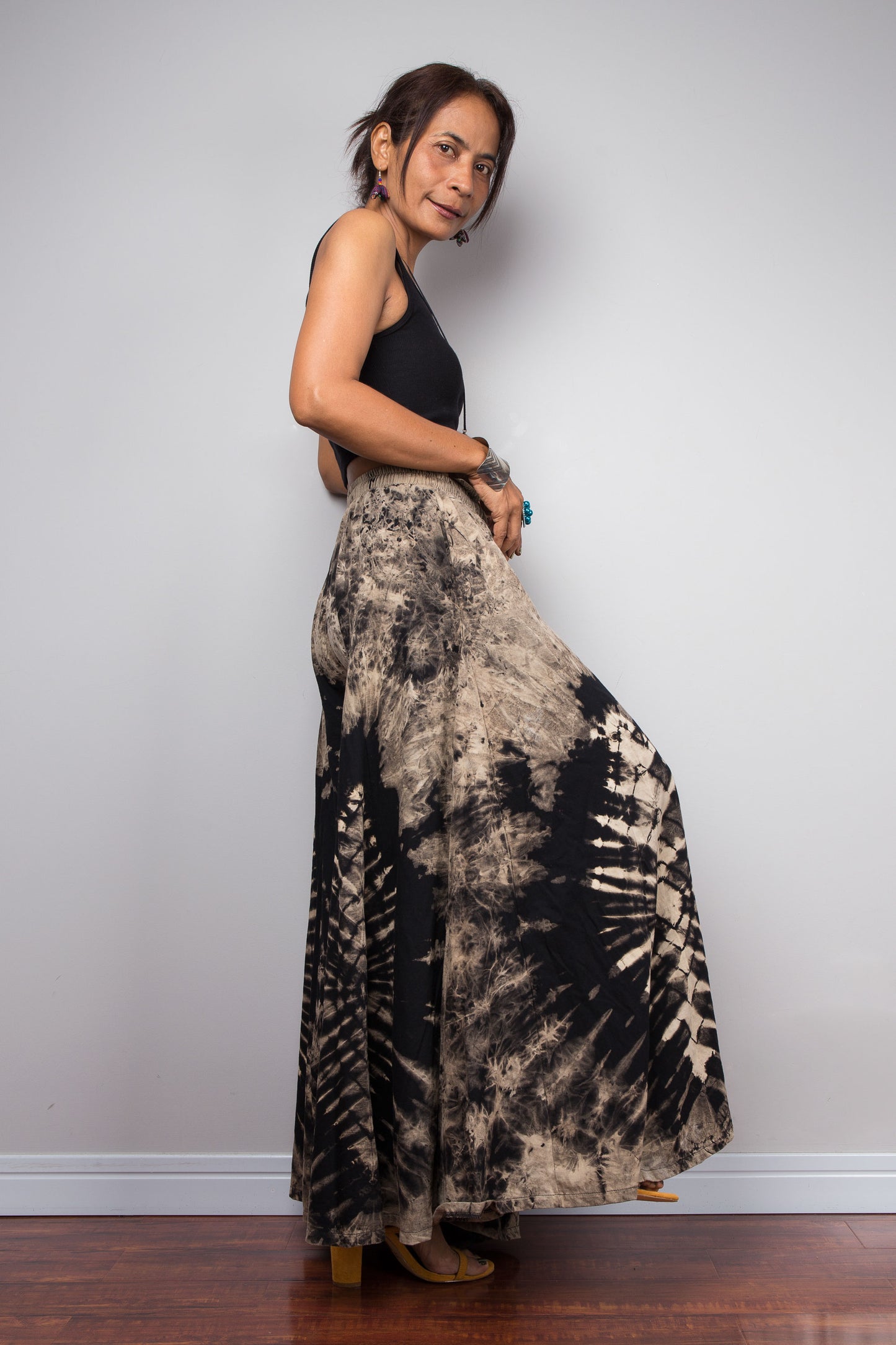 Side view of a model wearing the Nuichan reverse tie dye palazzo pants, showcasing the functional hidden side pocket and the fluid cotton drape of the ultra-wide leg silhouette in black and sand tones