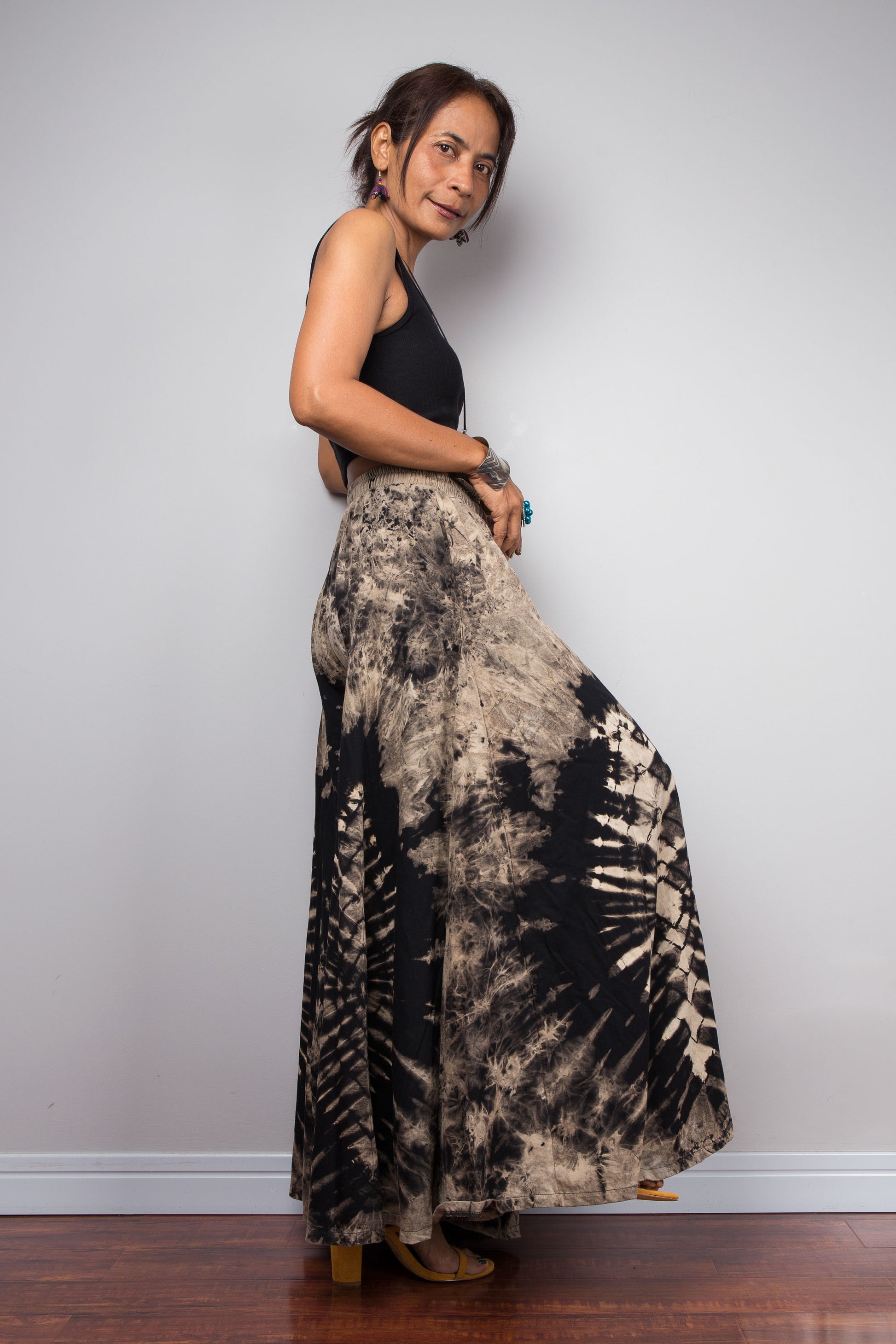Side view of a model wearing the Nuichan reverse tie dye palazzo pants, showcasing the functional hidden side pocket and the fluid cotton drape of the ultra-wide leg silhouette in black and sand tones