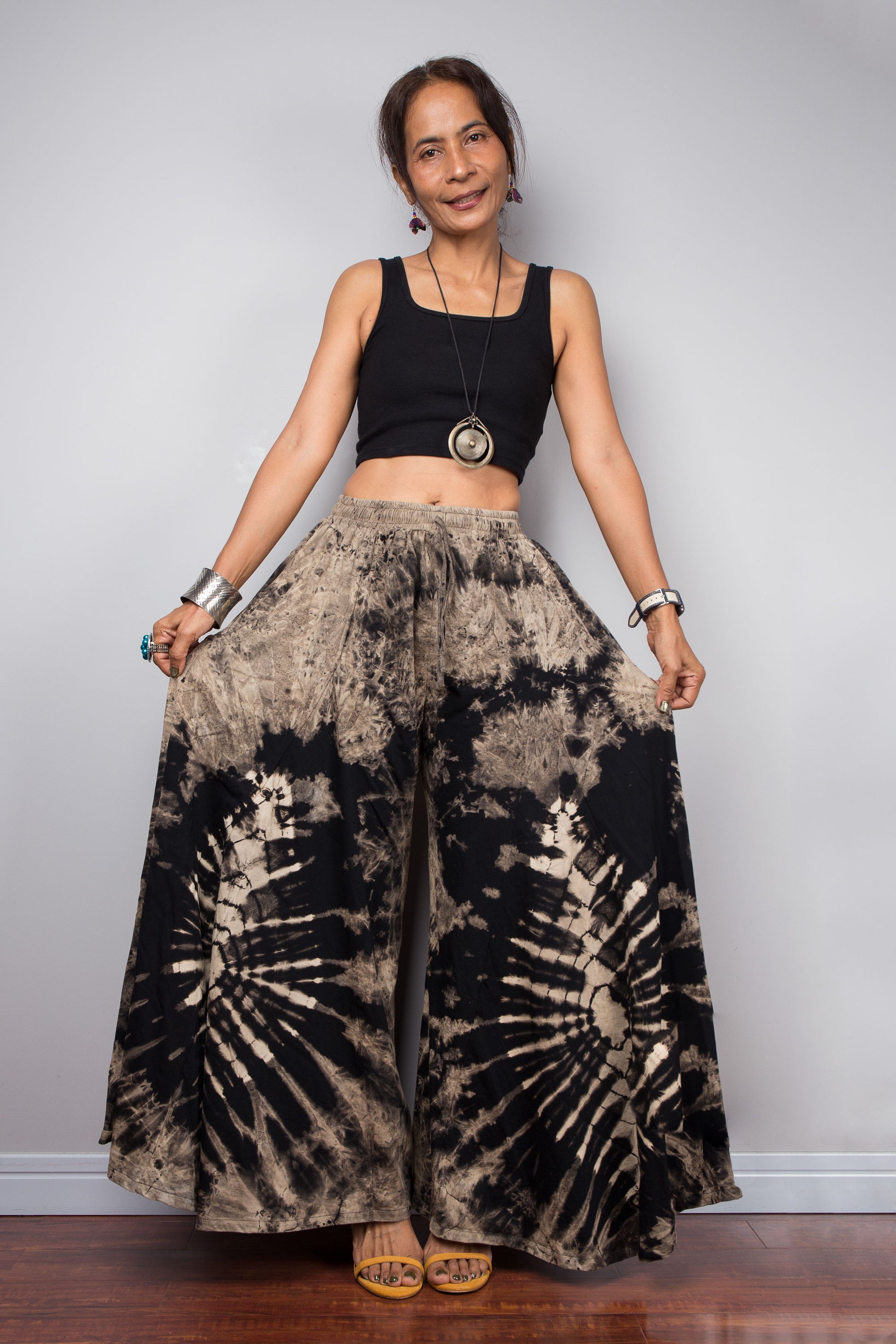 Dynamic pose of a model in the Nuichan black and sand reverse dye palazzo pants, illustrating the immense fabric volume and sweeping movement of the ultra-wide unstructured legs styled high-waisted