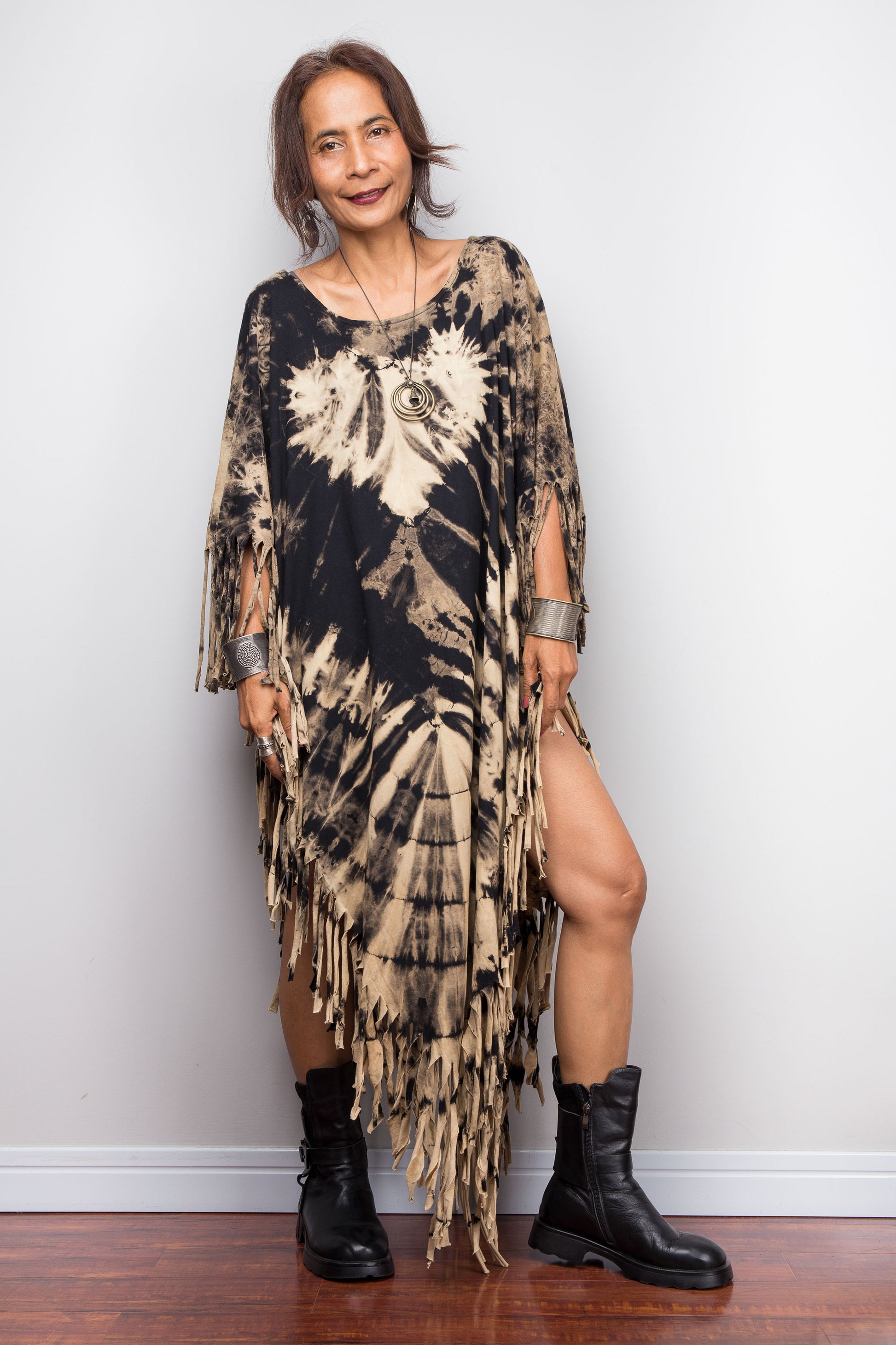 Woman wearing a unique Nuichan brand, reverse tie dye poncho tunic top dress with fringes against a plain background