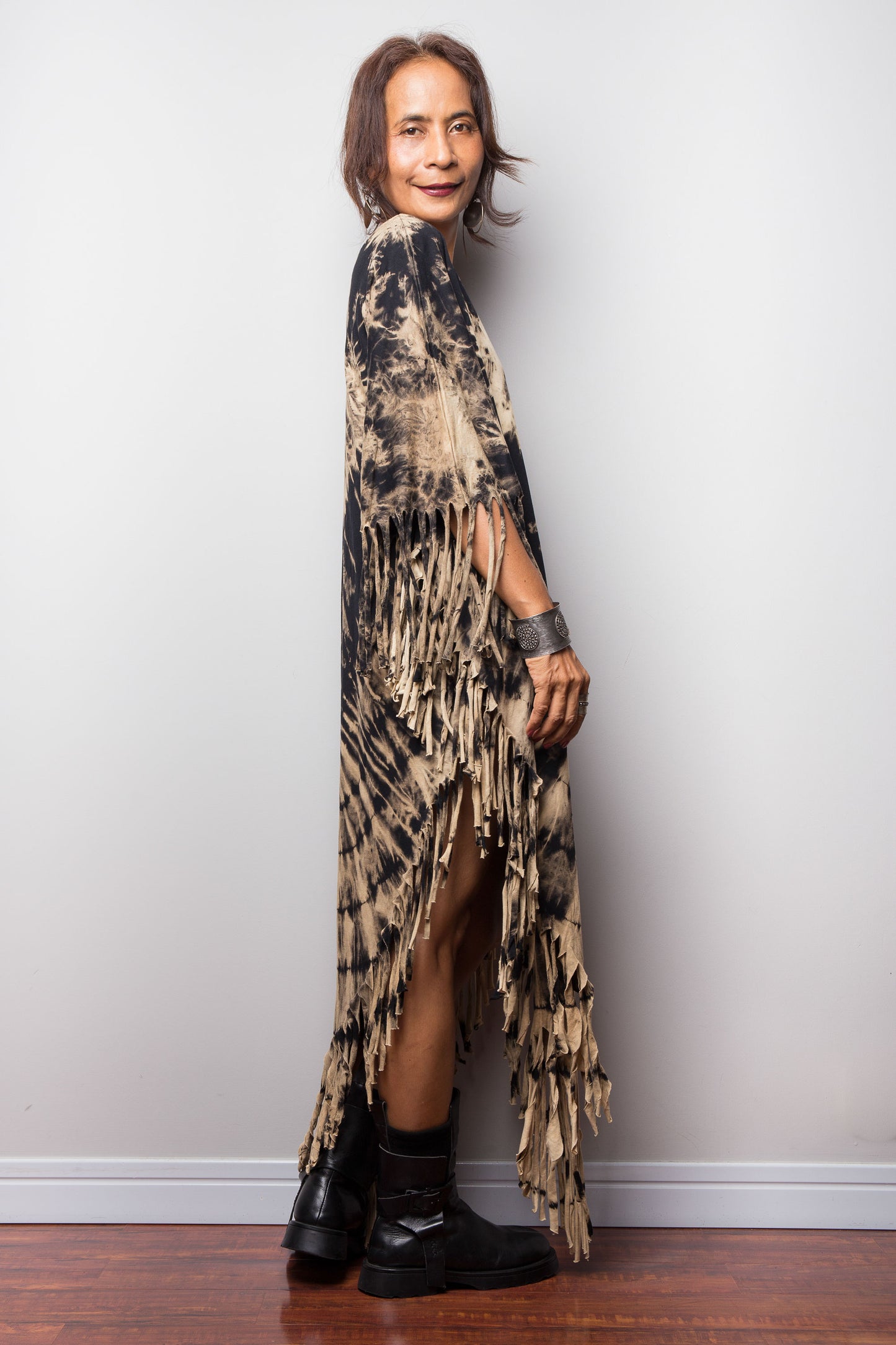 Woman wearing a long, reverse tie dye poncho dress with black shoes against a plain background