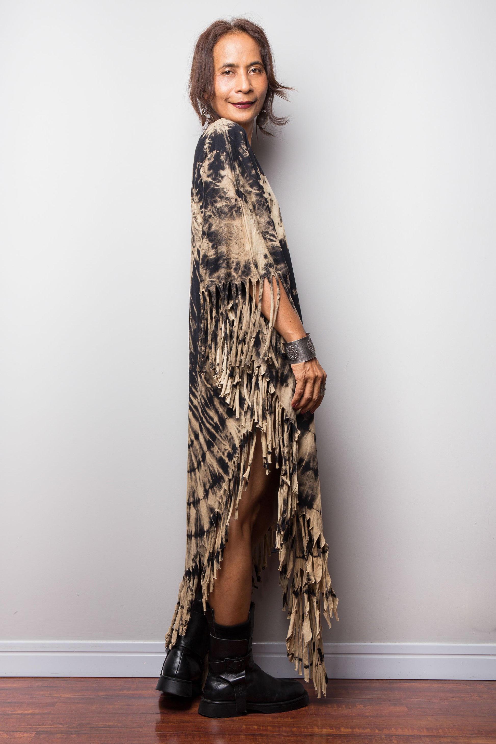 Woman wearing a long, reverse tie dye poncho dress with black shoes against a plain background