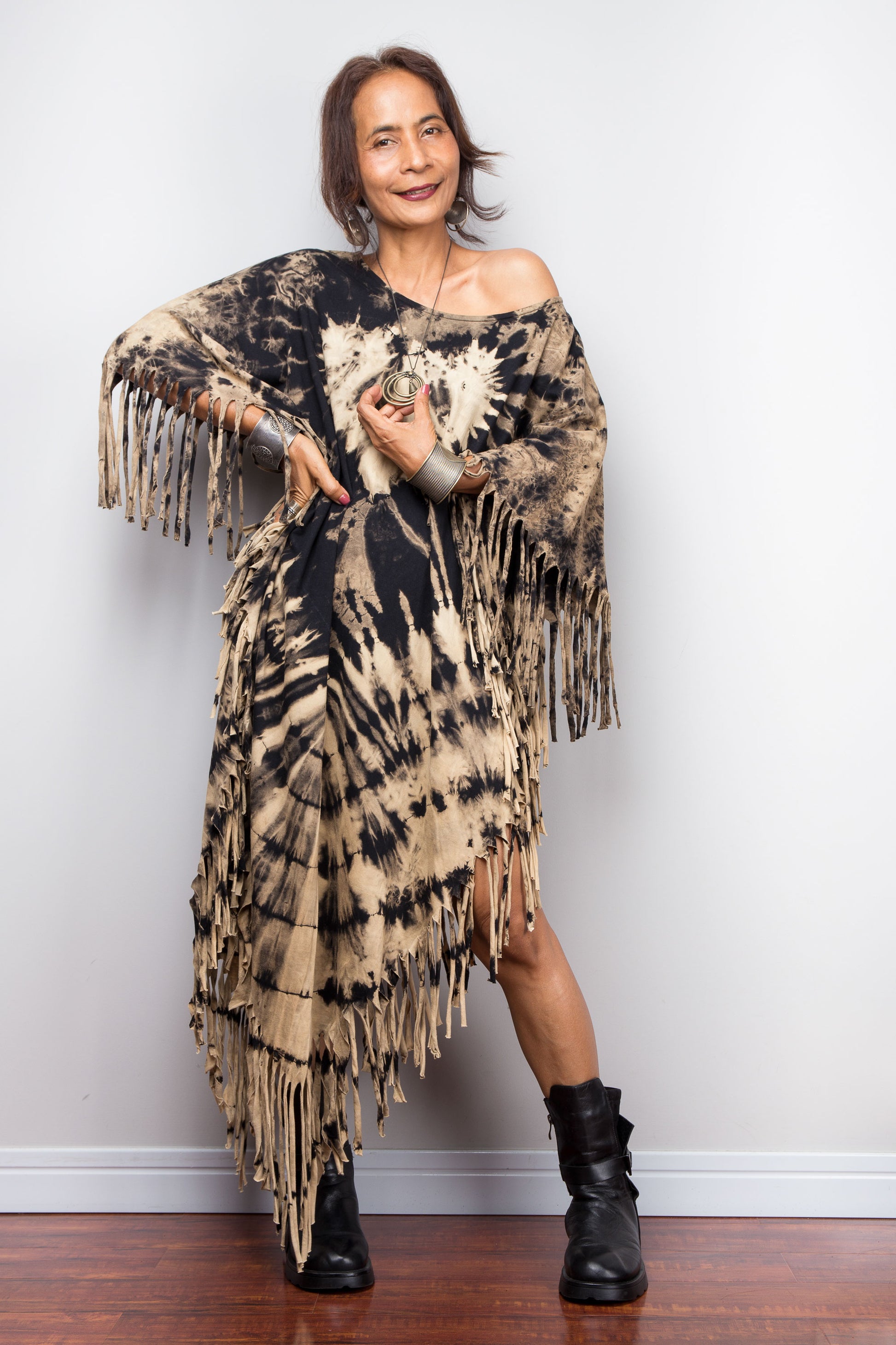 Petite Woman wearing a unique Nuichan brand, reverse tie dye poncho dress with fringes against a plain background