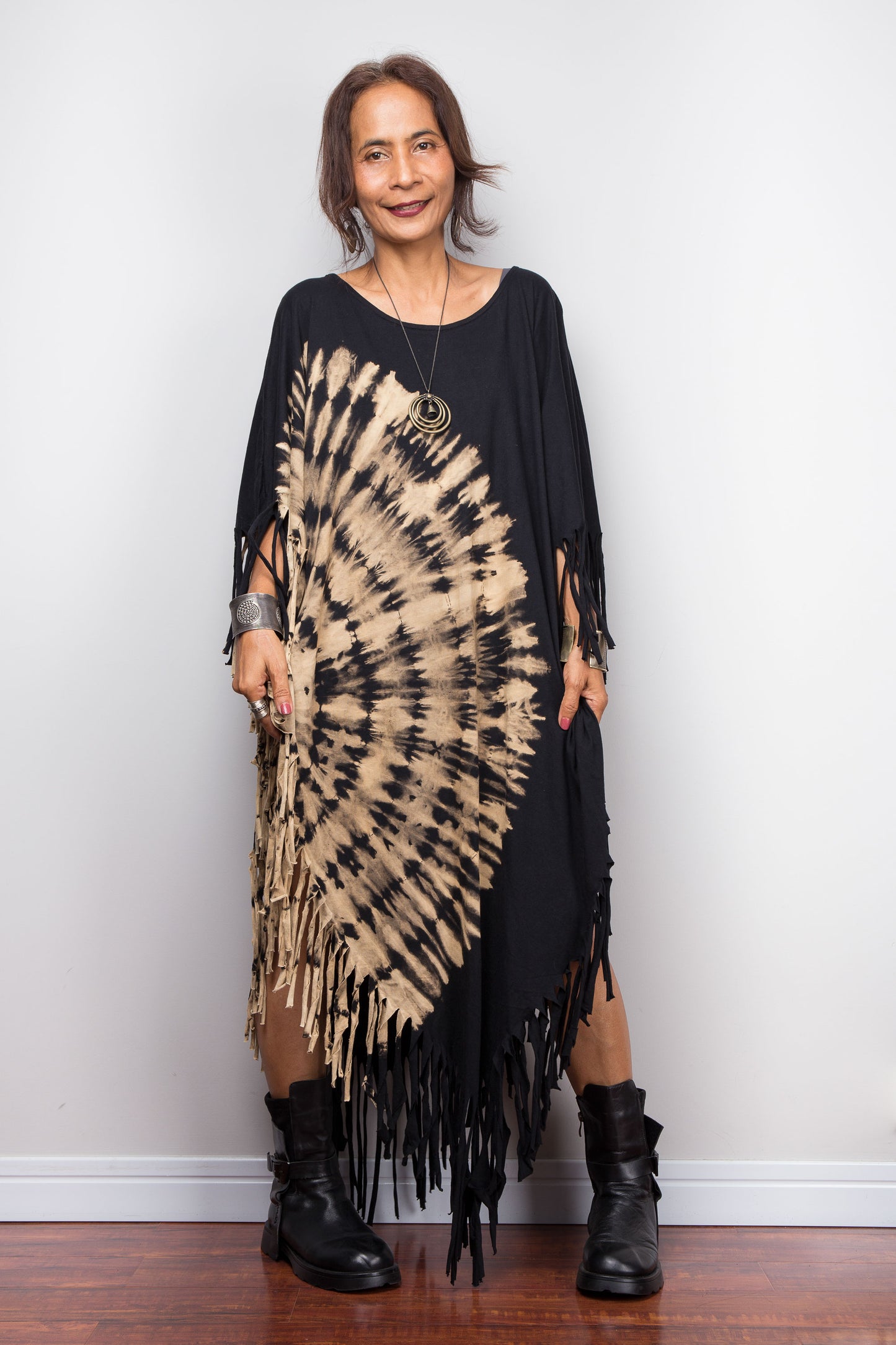 Petite Woman wearing an authentic Nuichan brand, black and beige tie-dye dress with fringe, standing against a white wall.