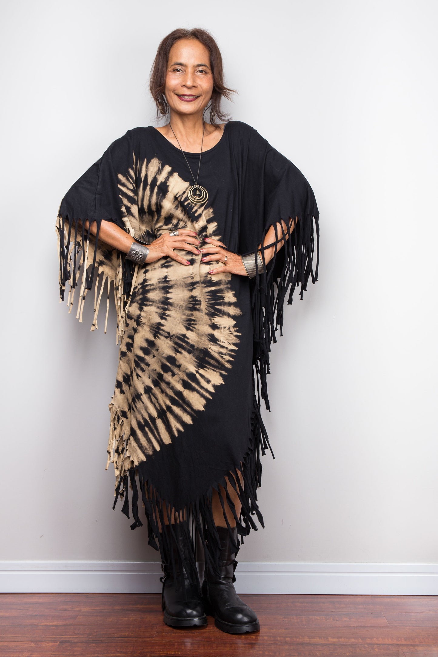 Petite Woman wearing a unique Nuichan brand, black and beige reverse tie dye poncho dress, against a white wall.