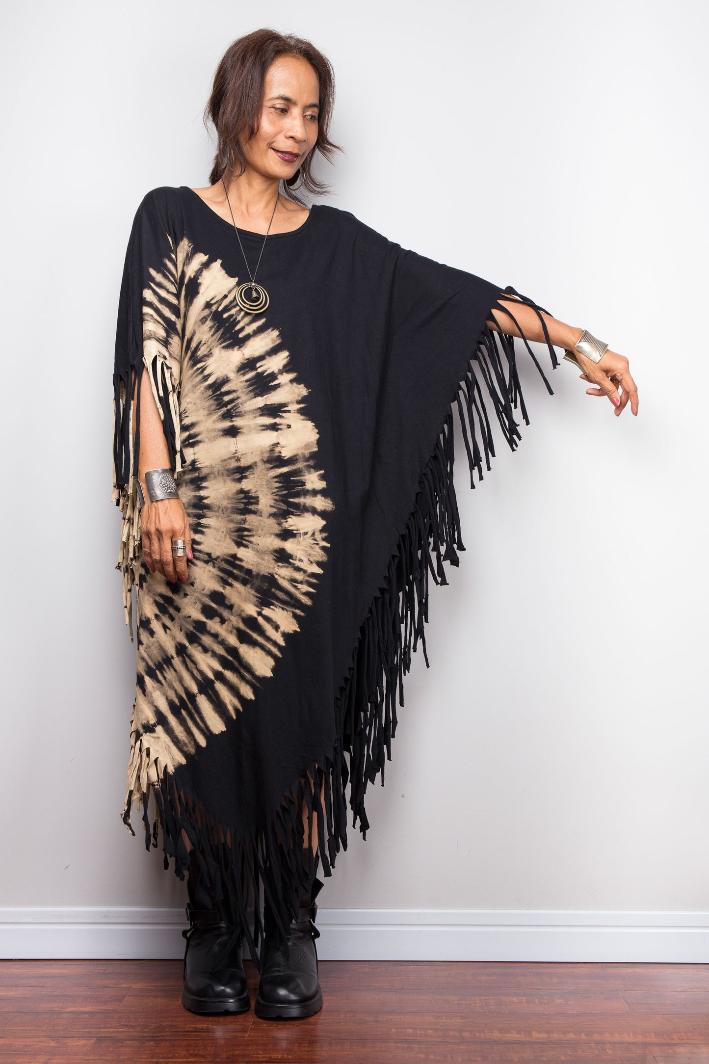 Woman wearing a black and beige Nuichan reverse tie dye poncho with fringe against a white wall.
