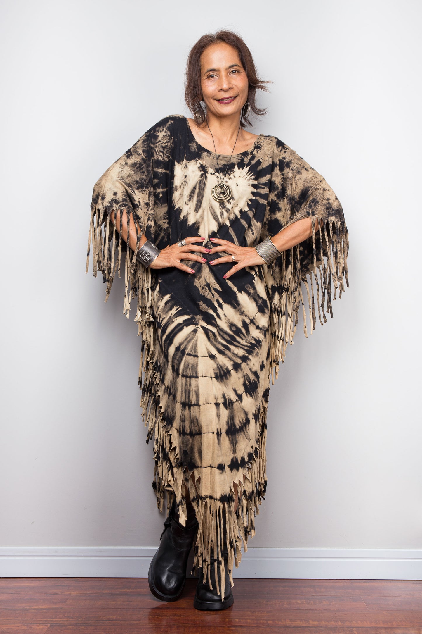 Woman wearing a unique Nuichan brand, reverse tie dye poncho dress with fringes against a plain background