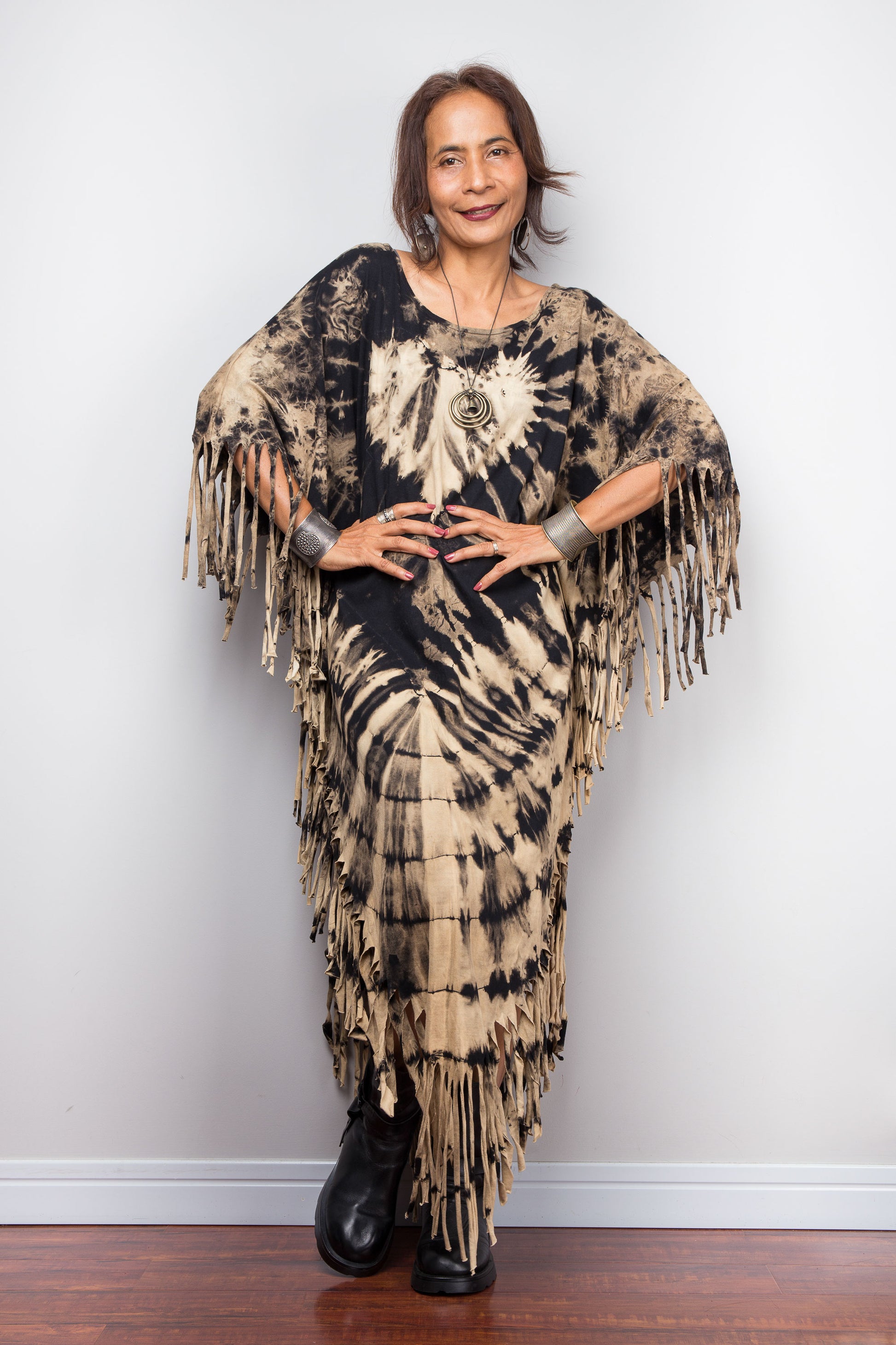 Woman wearing a unique Nuichan brand, reverse tie dye poncho dress with fringes against a plain background