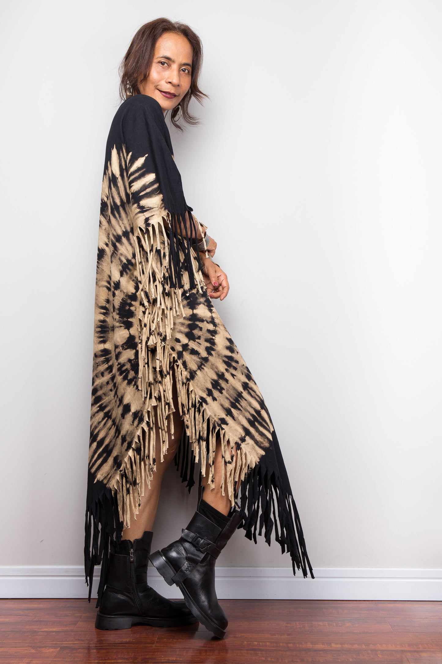 Woman wearing a reverse tie-dye fringe dress with black boots against a white wall.
