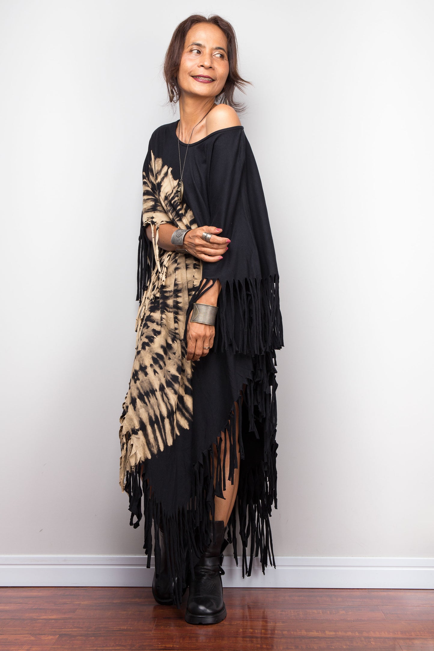 Petite Woman wearing an original Nuichan brand, black reverse tie dye poncho dress with fringe details against a white wall.