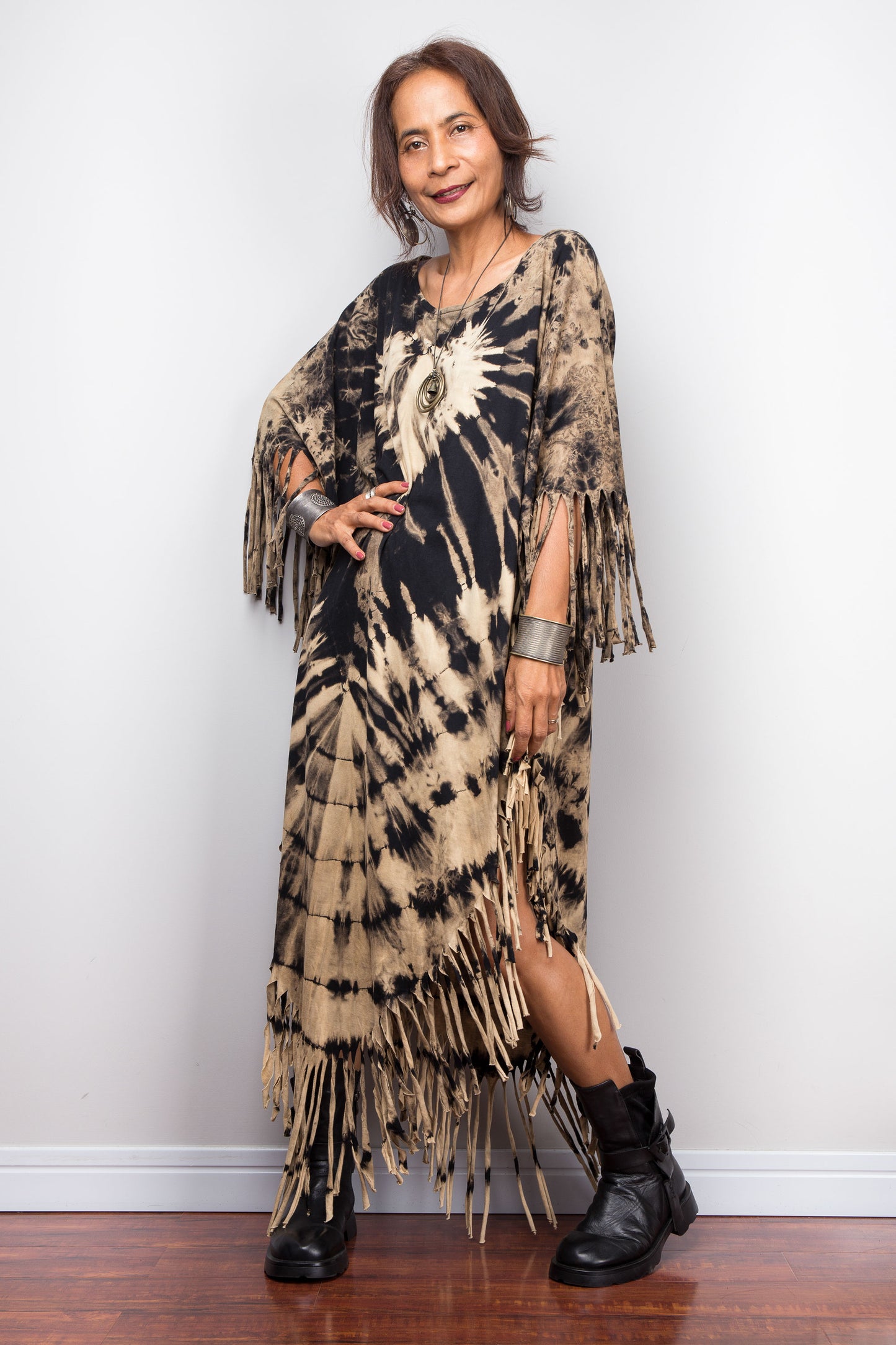 Woman wearing a reverse tie-dye dress with fringe details against a white wall.
